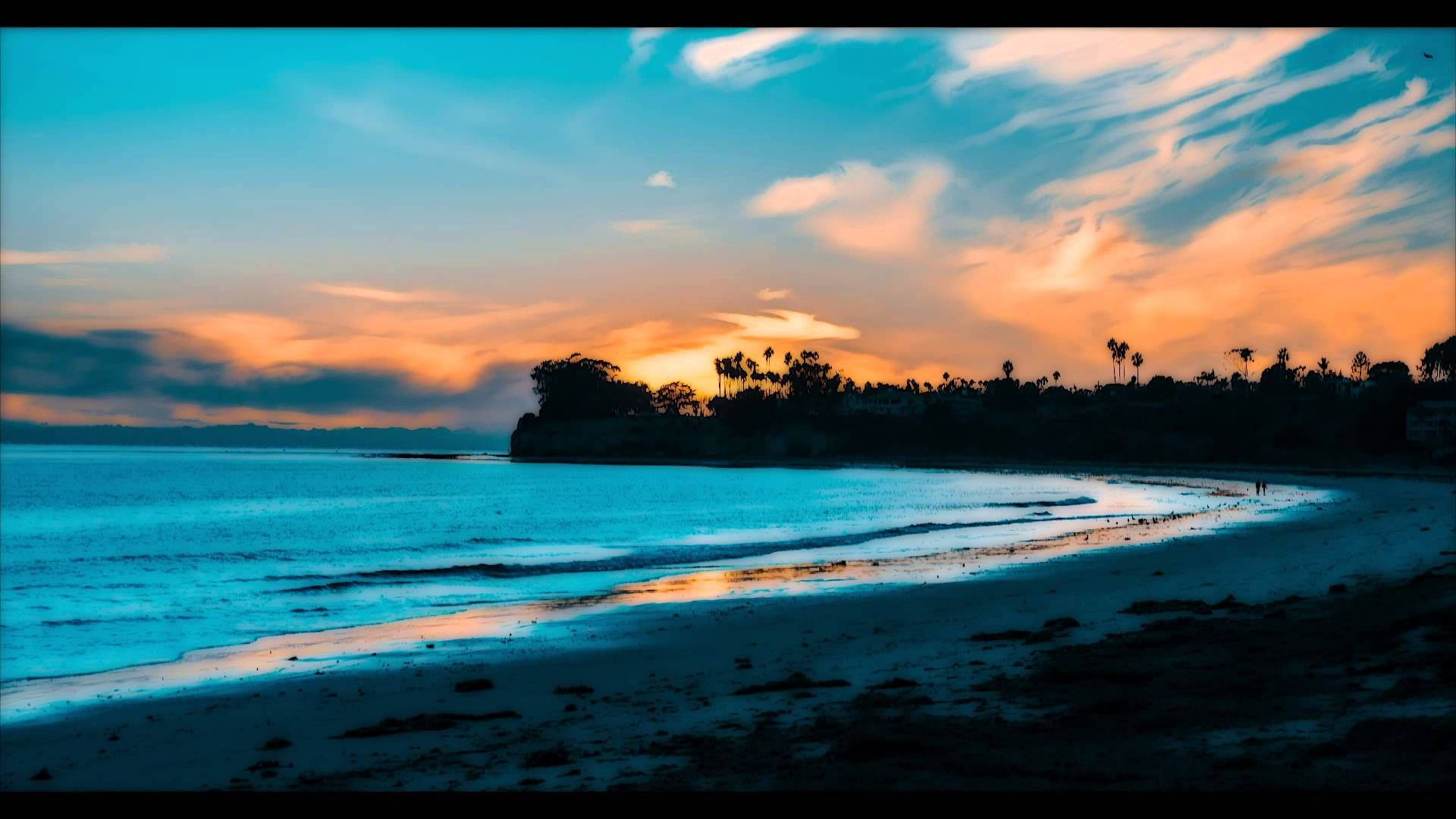 加州 桌布 壁紙 — 日落時分的寧靜海灘，鮮豔的橙色和藍色天空映照在平靜的水面和棕櫚樹的剪影上。
