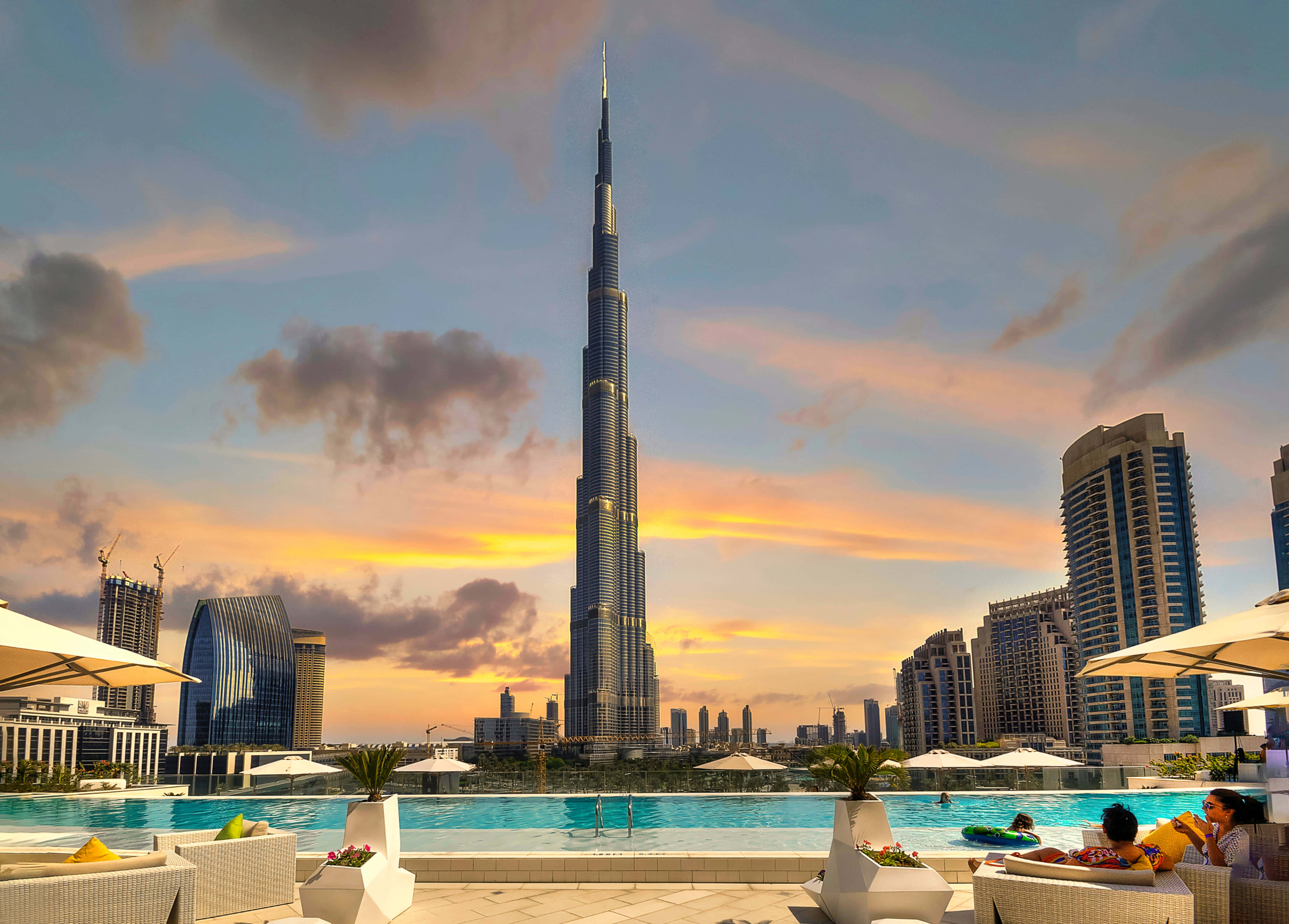 Burj Khalifa 桌布 壁紙 — 日落時分的屋頂泳池，哈里發塔高聳於杜拜天際線之上，客人在遮陽傘下放鬆。