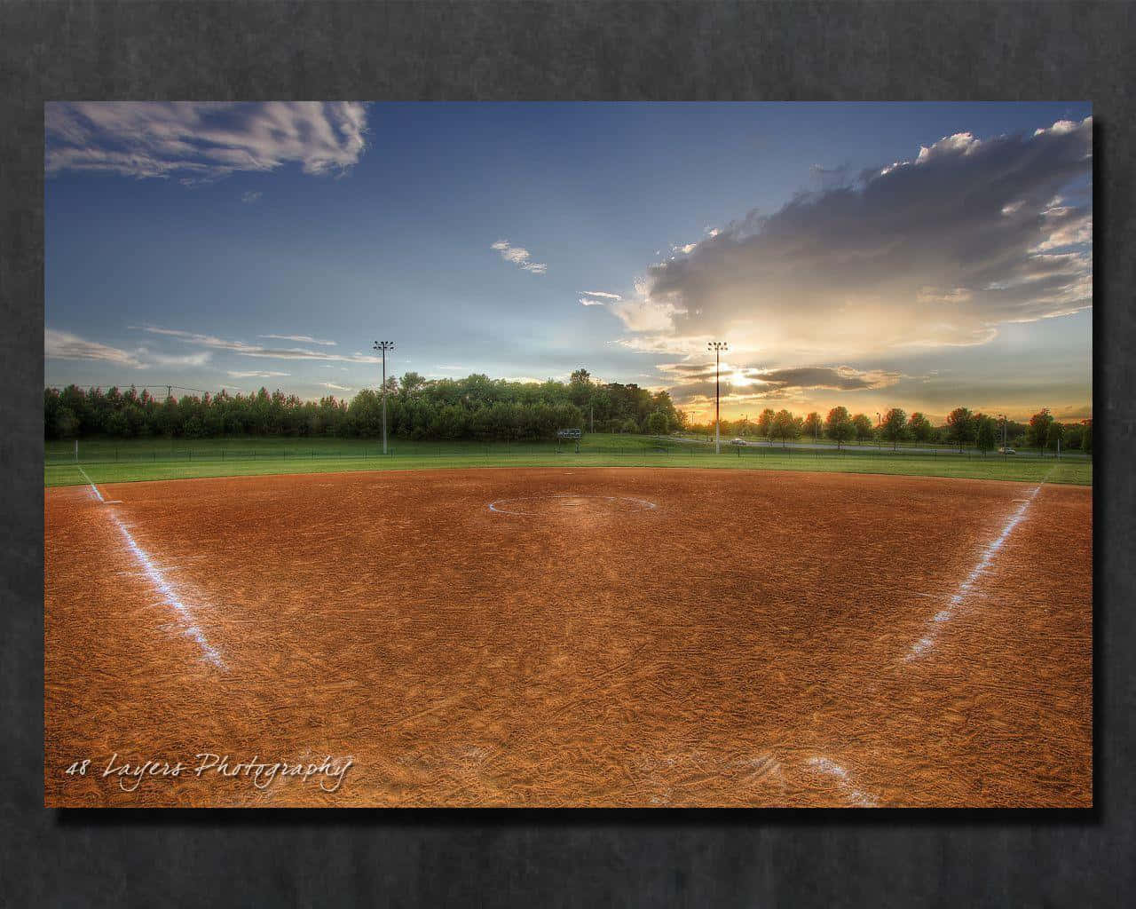 Baseball Field 桌布 壁紙 — 日落時分的棒球場，金色光芒照亮泥土內野和綠色外野，天空壯麗。