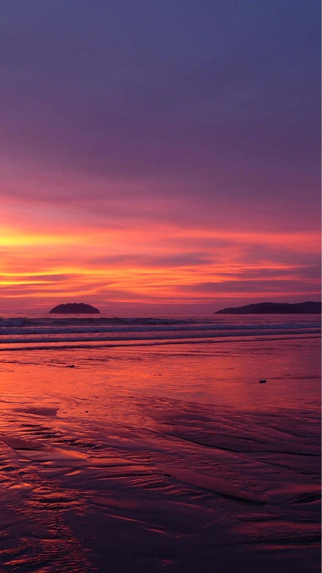 Sunset Beach iPhone 桌布 壁紙 — 日落時分的海灘，火紅橙和紫色的天空映照在濕沙和輕柔的海浪上。