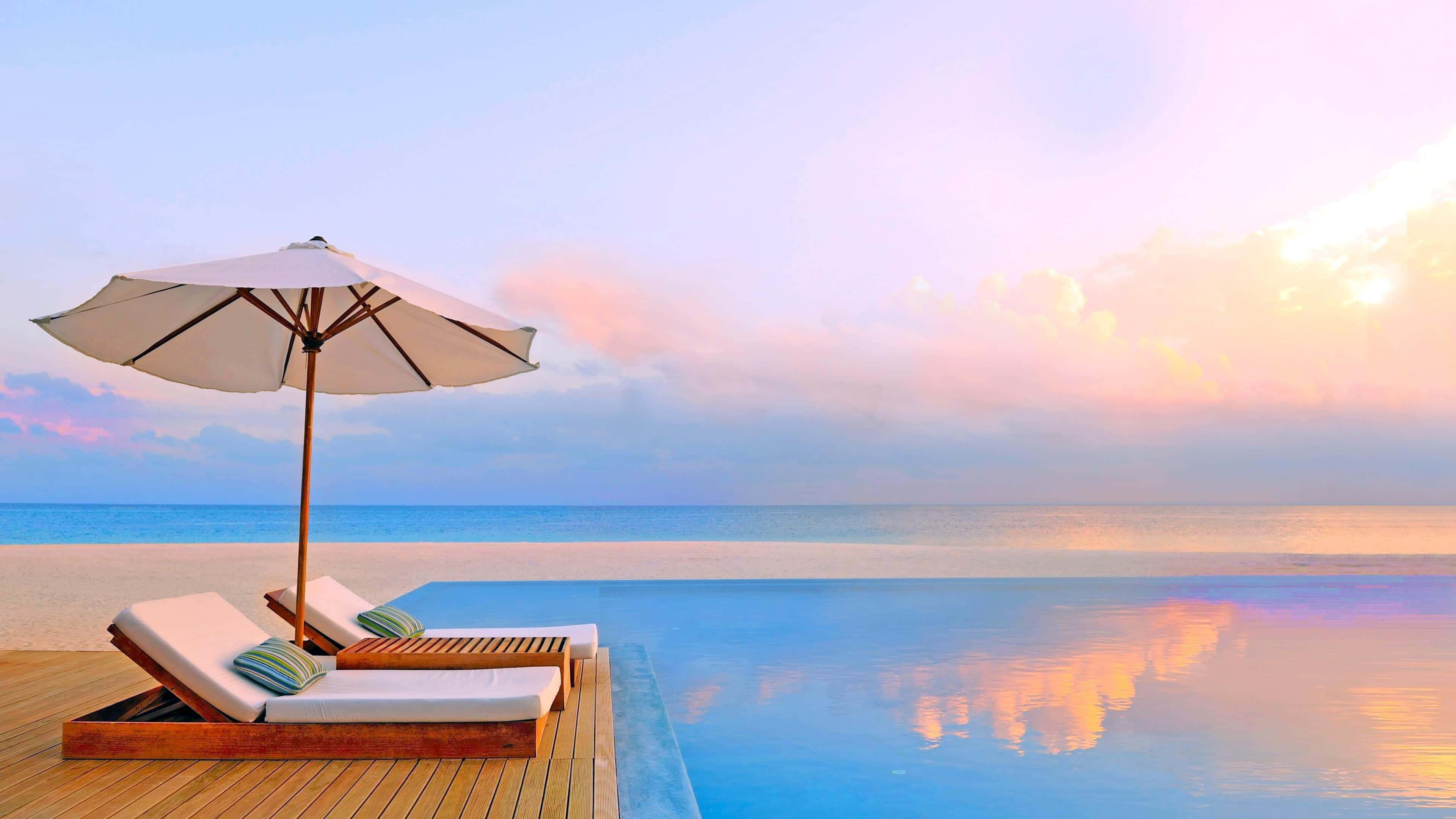 Maldives Beach 桌布 壁紙 — 日落時分的豪華無邊際泳池，配有躺椅和遮陽傘，俯瞰平靜的海平線。