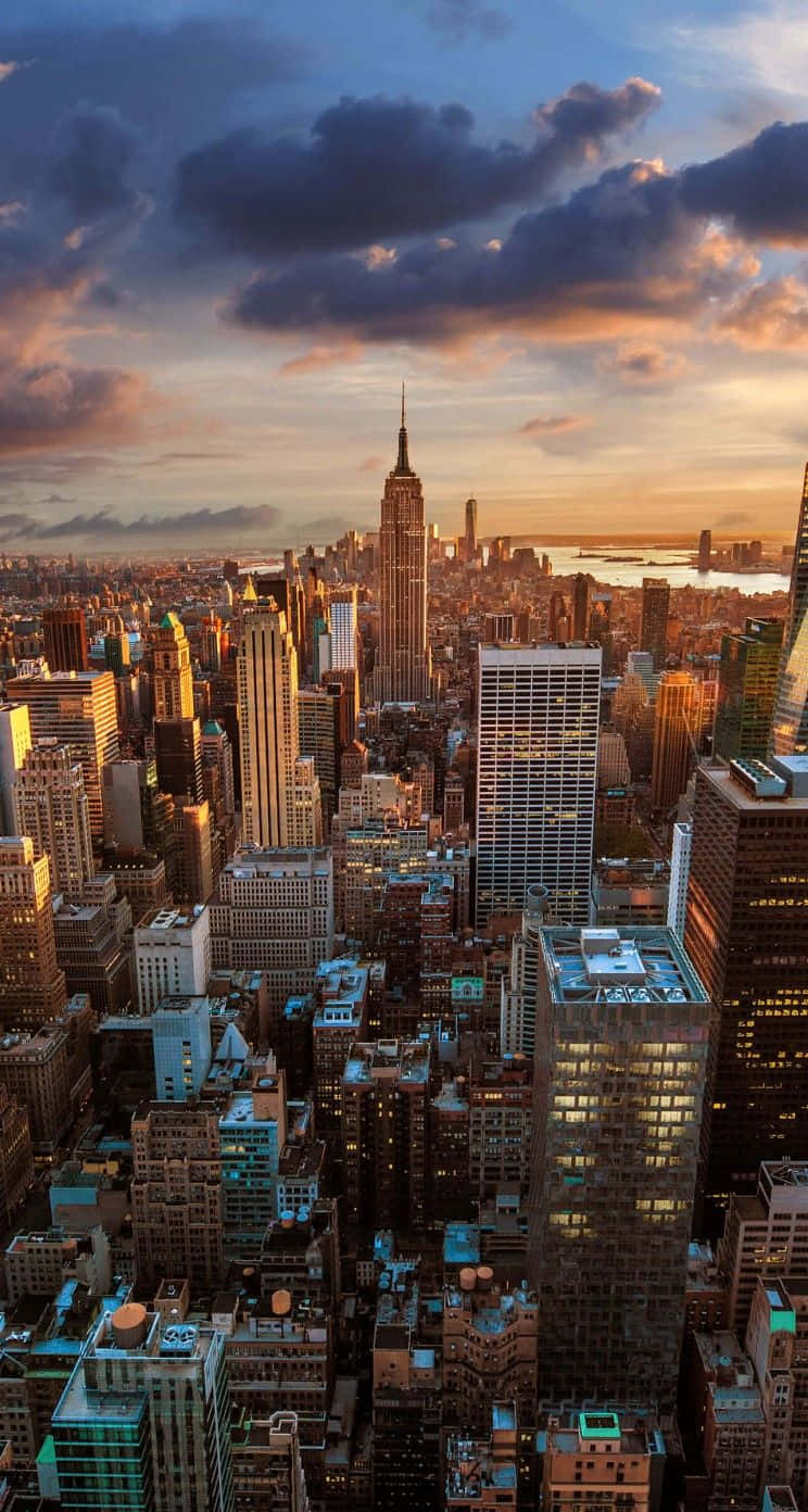 New York 桌布 壁紙 — 日落時分紐約市天際線的鳥瞰圖，帝國大廈聳立在密集的摩天大樓之上，雲朵呈現橙色和紫色光芒。