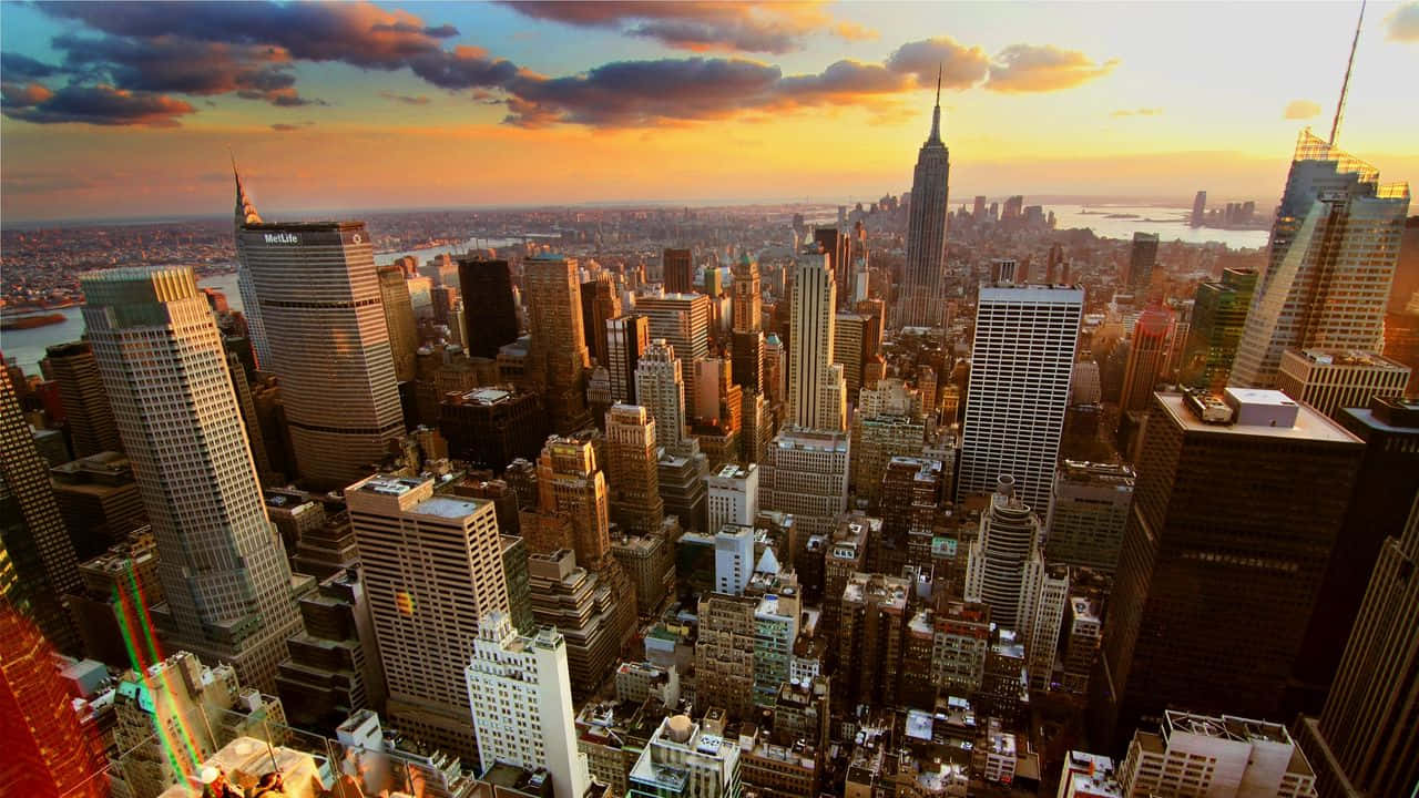 720p Empire State Building 桌布 壁紙 — 日落時分紐約市天際線的鳥瞰圖，金色光芒照亮摩天大樓和雲層。