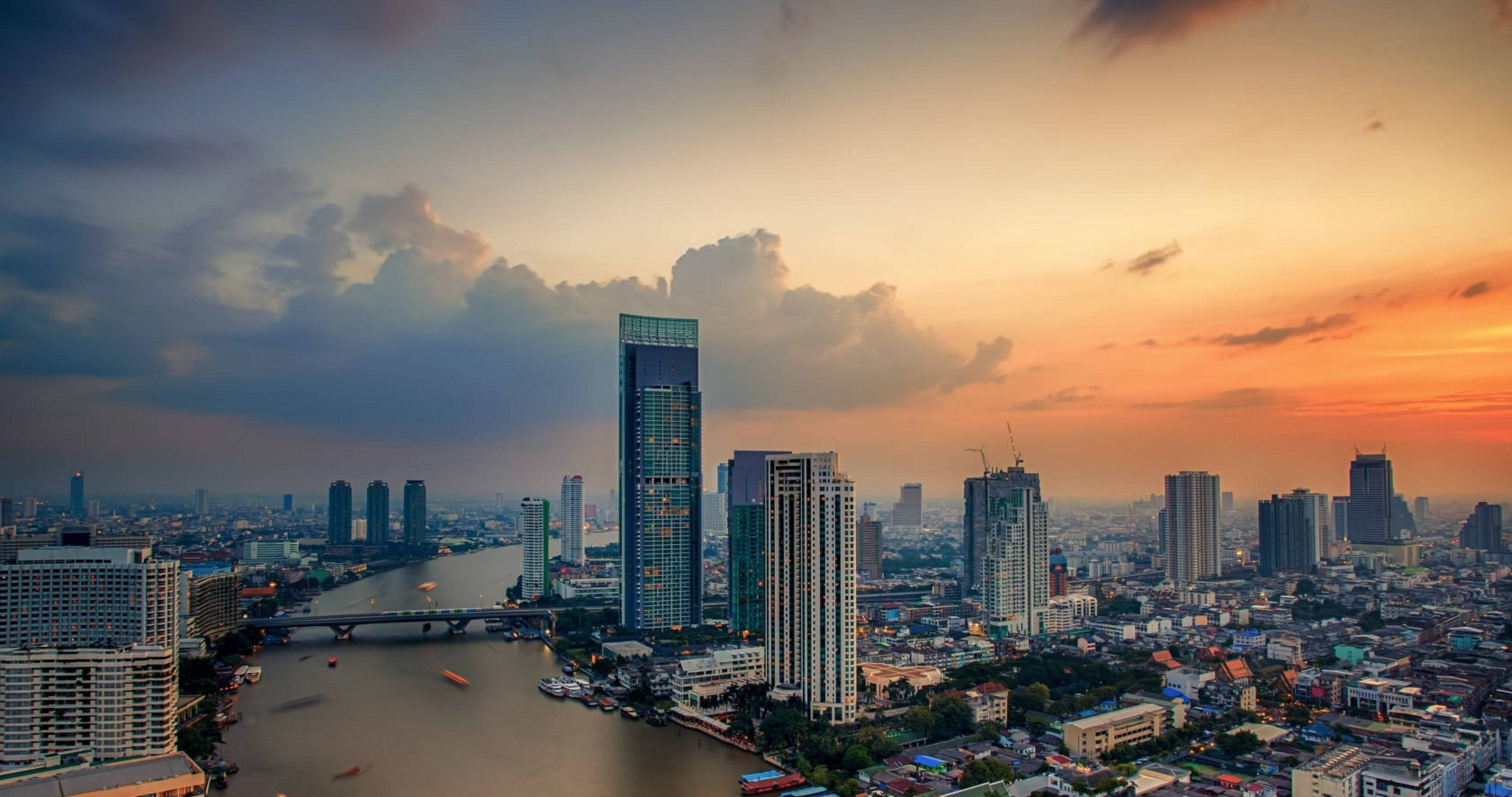 Bangkok 桌布 壁紙 — 日落時分繁忙城市天際線的鳥瞰圖，一條寬闊的河流流經現代摩天大樓和低層建築。