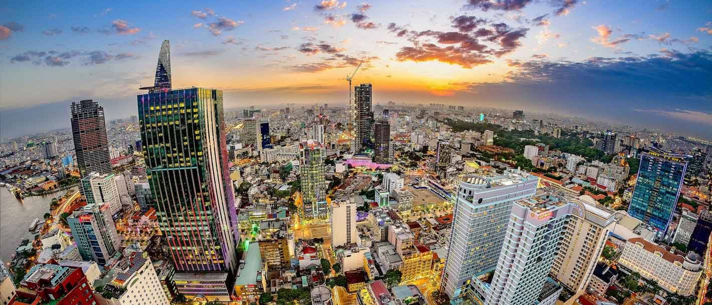 Ho Chi Minh City 桌布 壁紙 — 日落時分繁忙城市景觀的鳥瞰圖，高聳的摩天大樓和閃爍的燈光映襯著充滿活力的橙色和紫色天空。