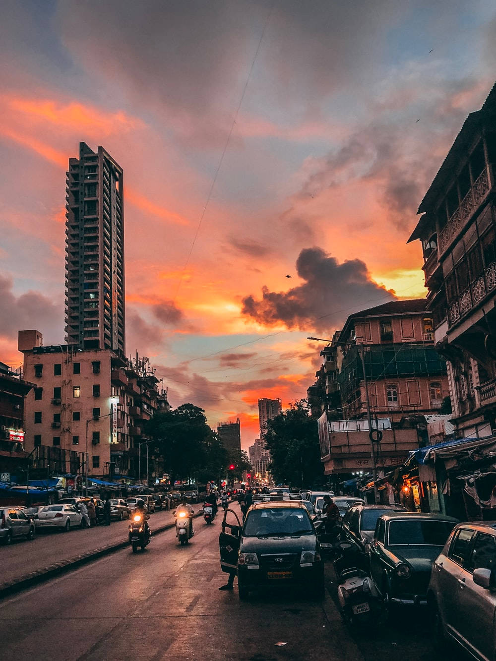 Indian 桌布 壁紙 — 日落時分繁忙的城市街道，鮮豔的橙色雲朵高聳於混合建築和行駛中的車輛之上。
