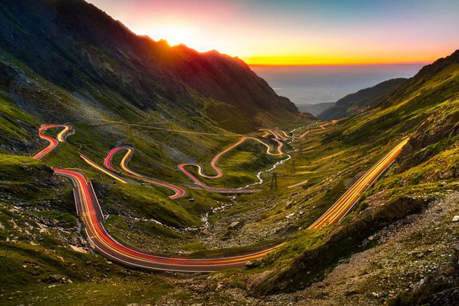Romania 桌布 壁紙 — 日落時分蜿蜒的山路，發光的汽車軌跡蜿蜒穿過翠綠的山谷。