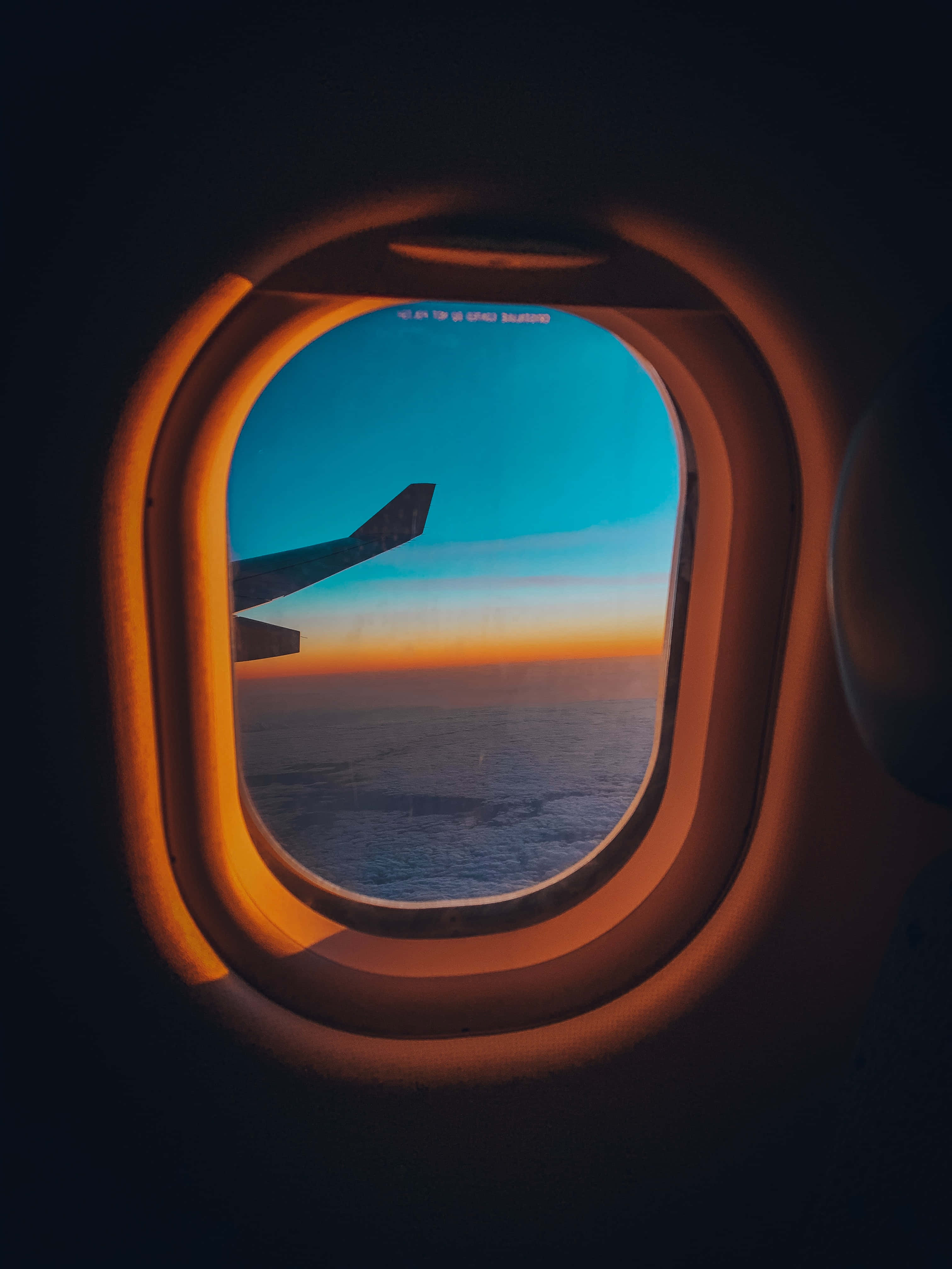 Airplane Window 桌布 壁紙 — 日落時從飛機窗戶看到的景色，顯示機翼、海洋和漸變天空，被溫暖的機艙光芒框住。