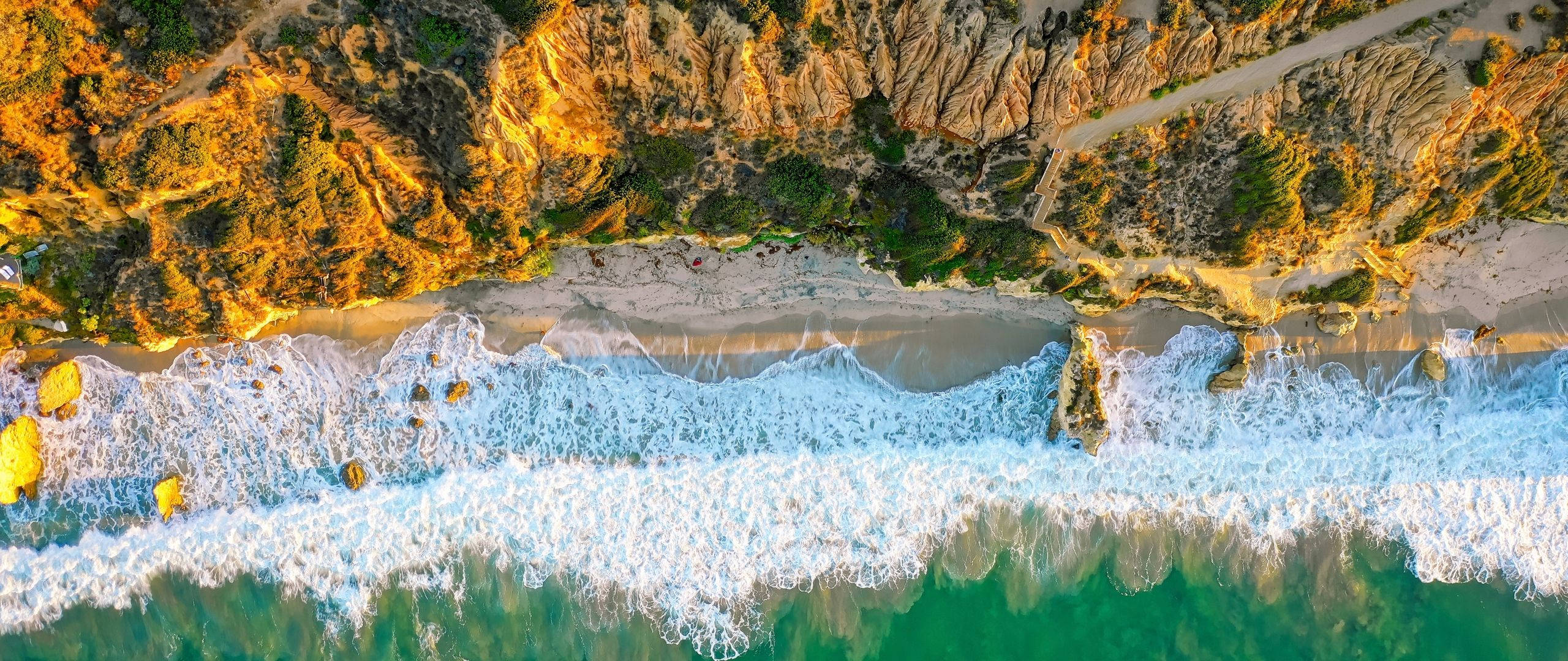 Malibu 桌布 壁紙 — 日落時金色懸崖與碧綠海洋波浪交匯的鳥瞰圖，下方有沙灘。