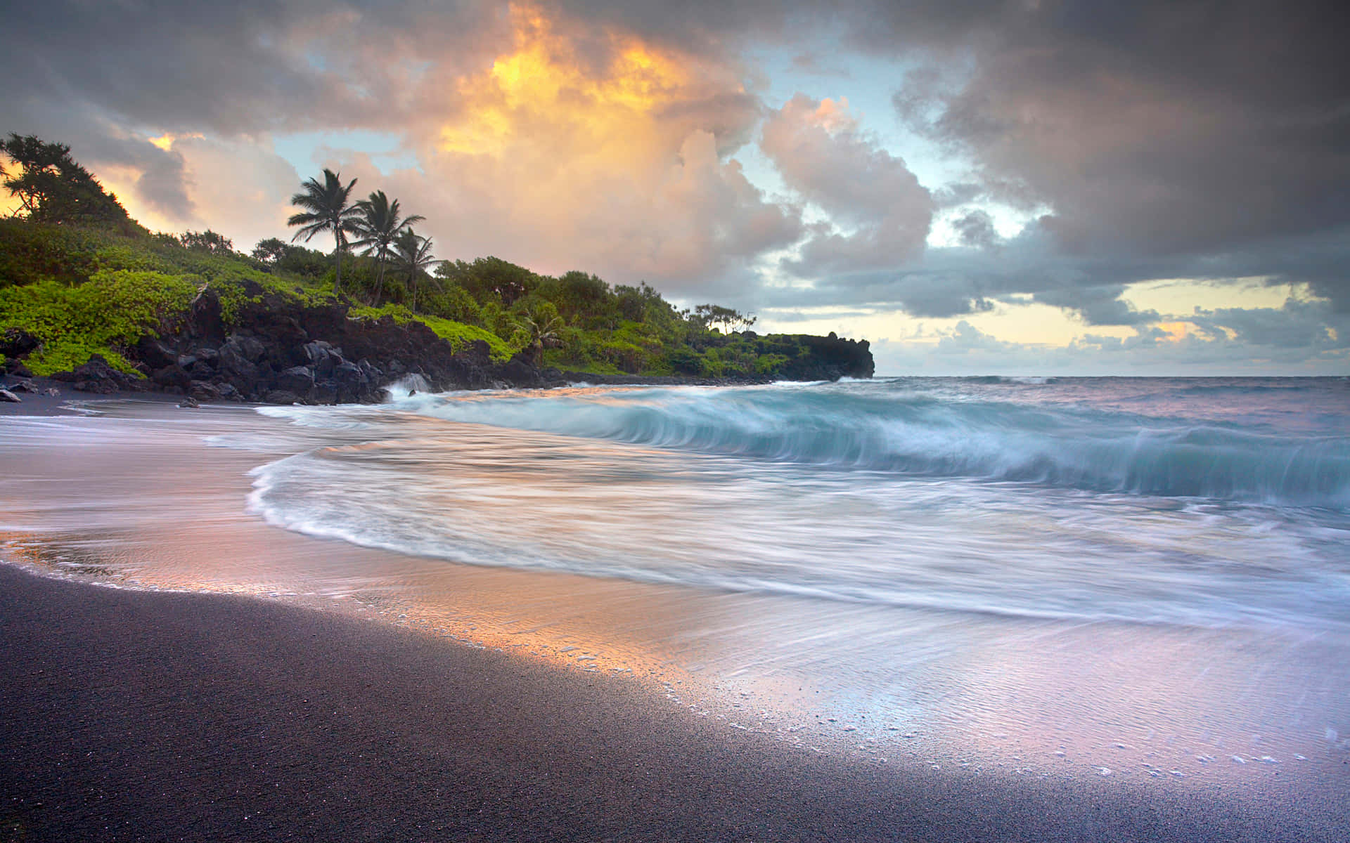 Black Sand Beach 桌布 壁紙 — 日落繪出戲劇性的雲彩，籠罩著黑沙灘，碧綠的海浪拍打著長滿棕櫚樹的茂密綠色懸崖。