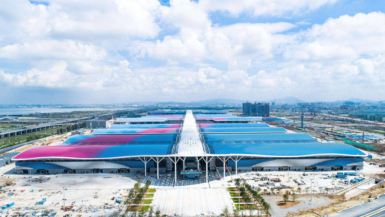 Shenzhen 桌布 壁紙 — 明亮多雲天空下，未來主義體育場的鳥瞰圖，帶有充滿活力的藍色和粉紅色屋頂面板。
