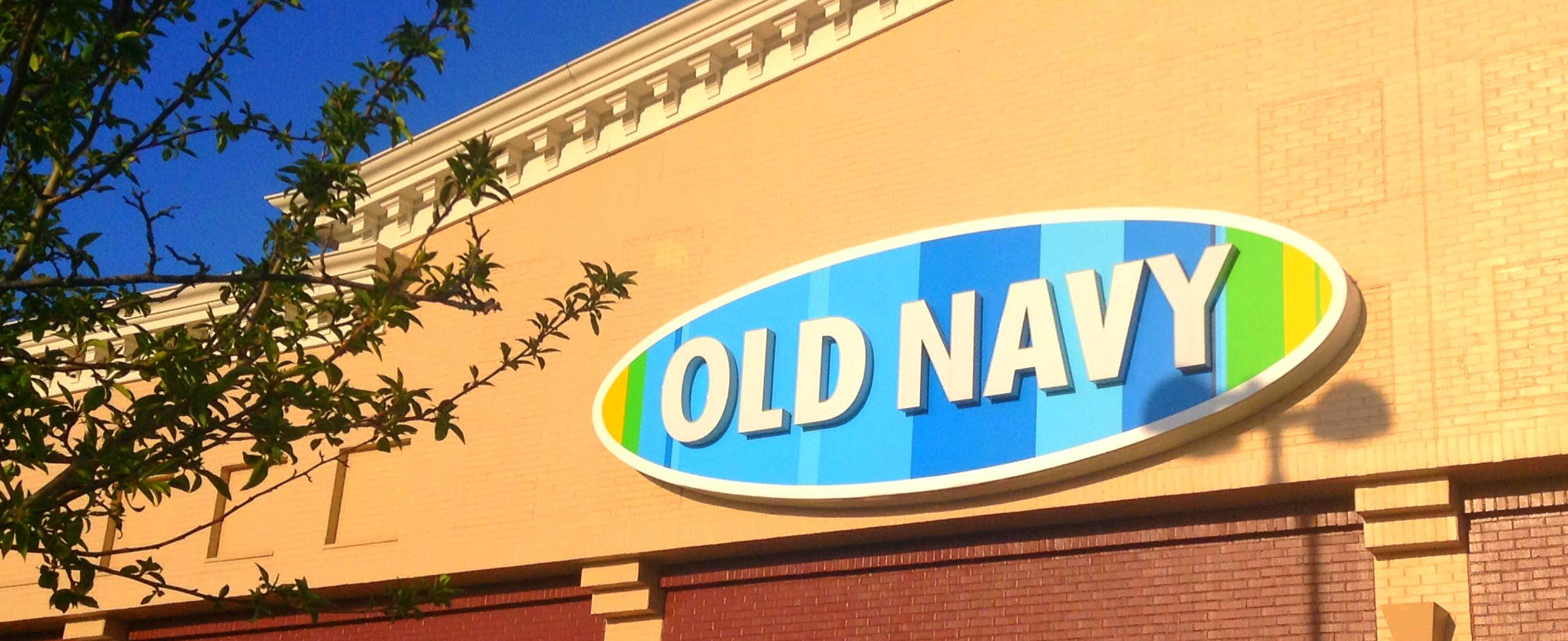 old 桌布 壁紙 — 明亮的 Old Navy 商店招牌帶有彩虹條紋，在晴朗的藍天下，映襯著陽光普照的黃色建築物。