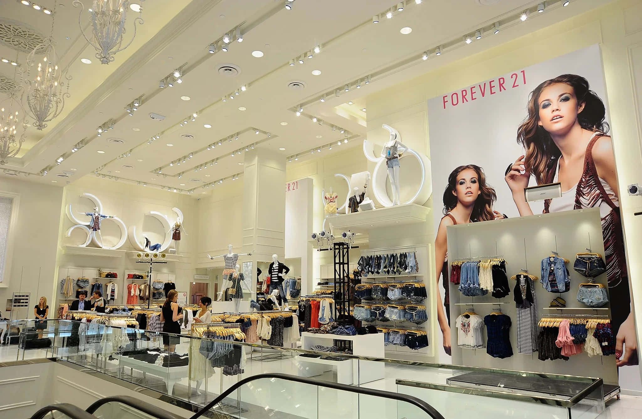 永遠21 桌布 壁紙 — 明亮的Forever 21店鋪內部，配有白色裝飾、玻璃欄杆和展示模特兒的大型時尚海報。