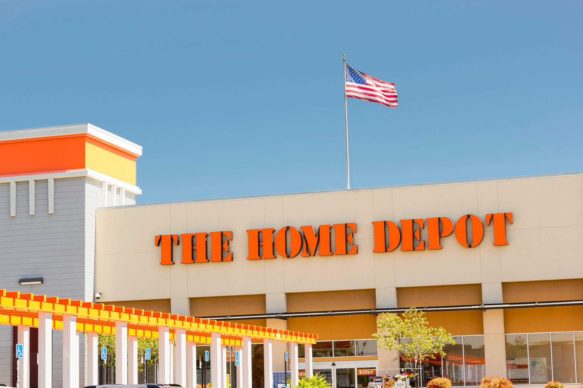 Home Depot 桌布 壁紙 — 明亮的Home Depot商店，帶有橙色標牌和美國國旗在清澈的藍天下飄揚。