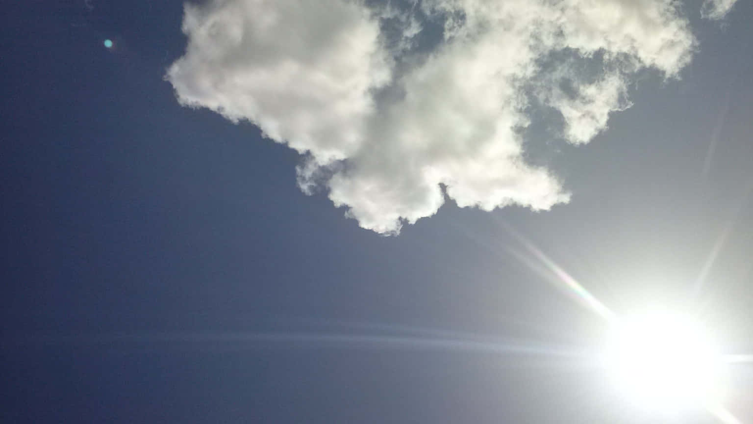 SUN-1 壁紙 — 明亮的太陽穿過蓬鬆的白雲，在深藍色的天空中帶有鏡頭光暈。