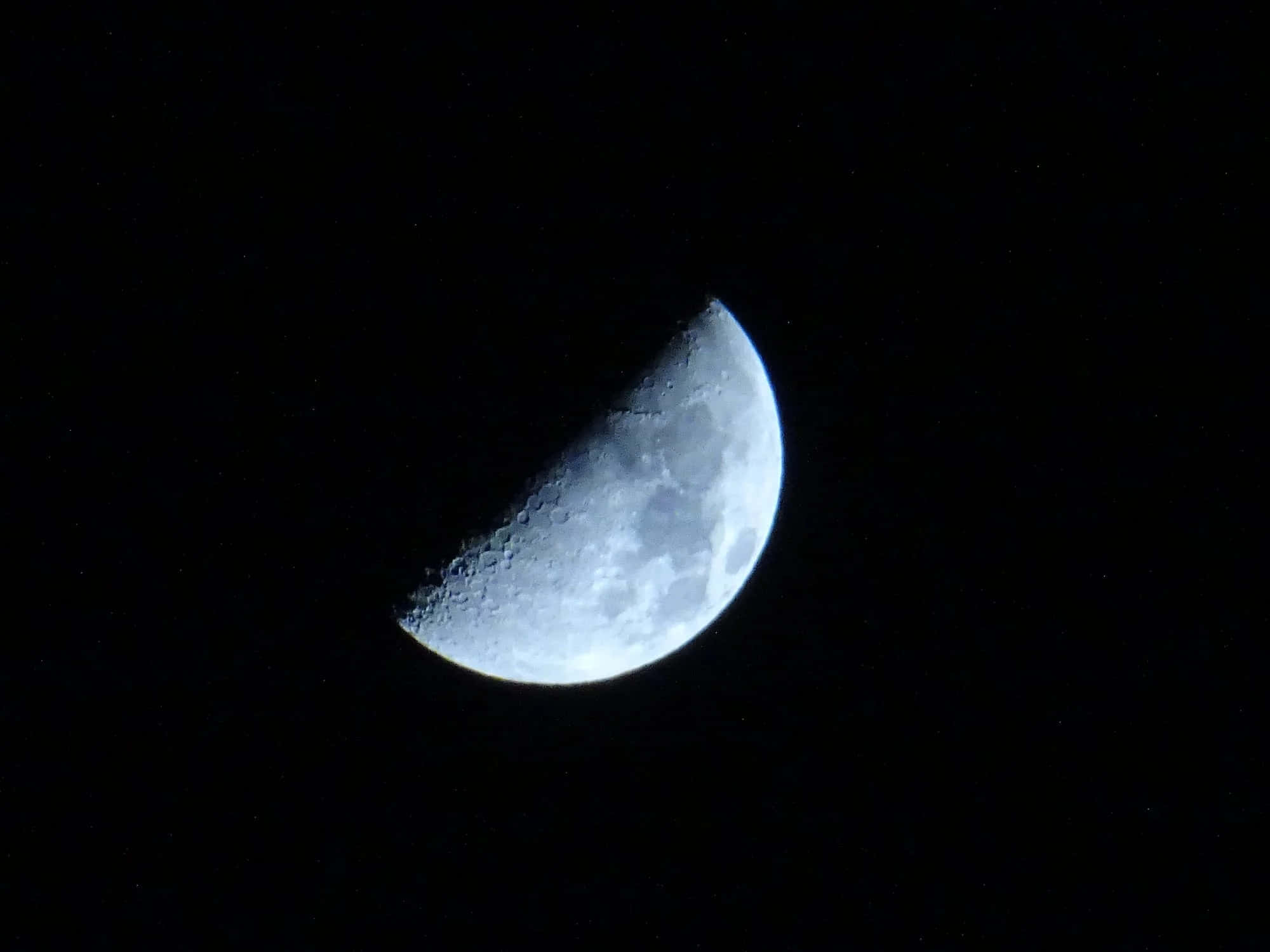 Half Moon 桌布 壁紙 — 明亮的彎月在佈滿星星的黑色天空中發光，可見隕石坑和月海。