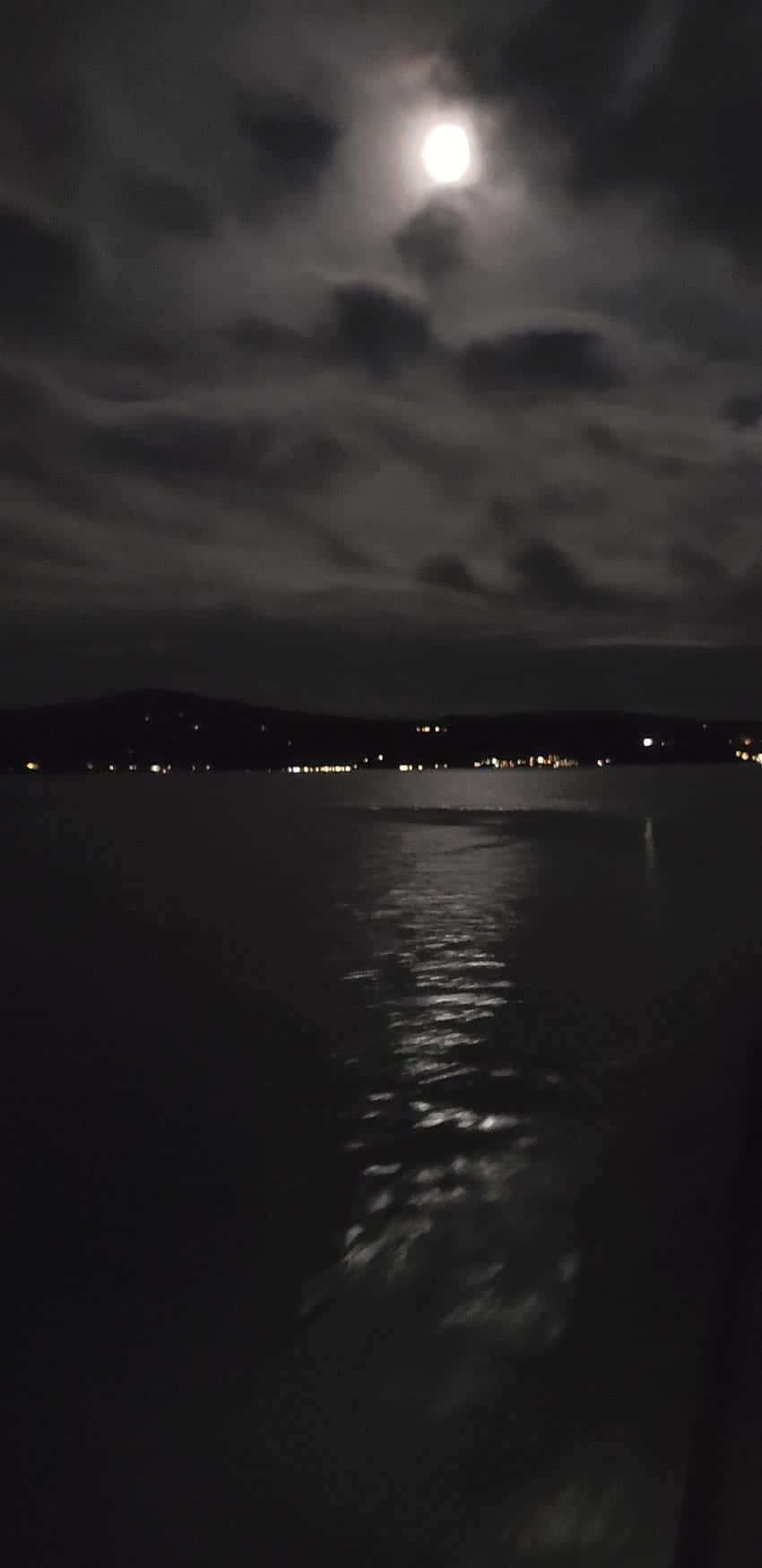 暗黑風格 桌布 壁紙 — 明亮的月亮穿過多雲的天空照耀在黑暗的水面上，反射出遠處的城市燈光。