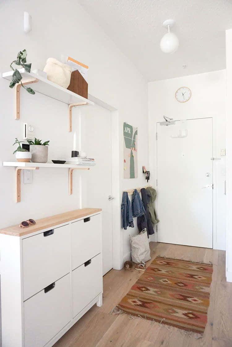 Minimalist Design 桌布 壁紙 — 明亮的極簡主義走廊，白色牆壁、木質層架、盆栽植物和一條圖案地毯，通往一扇白色門。