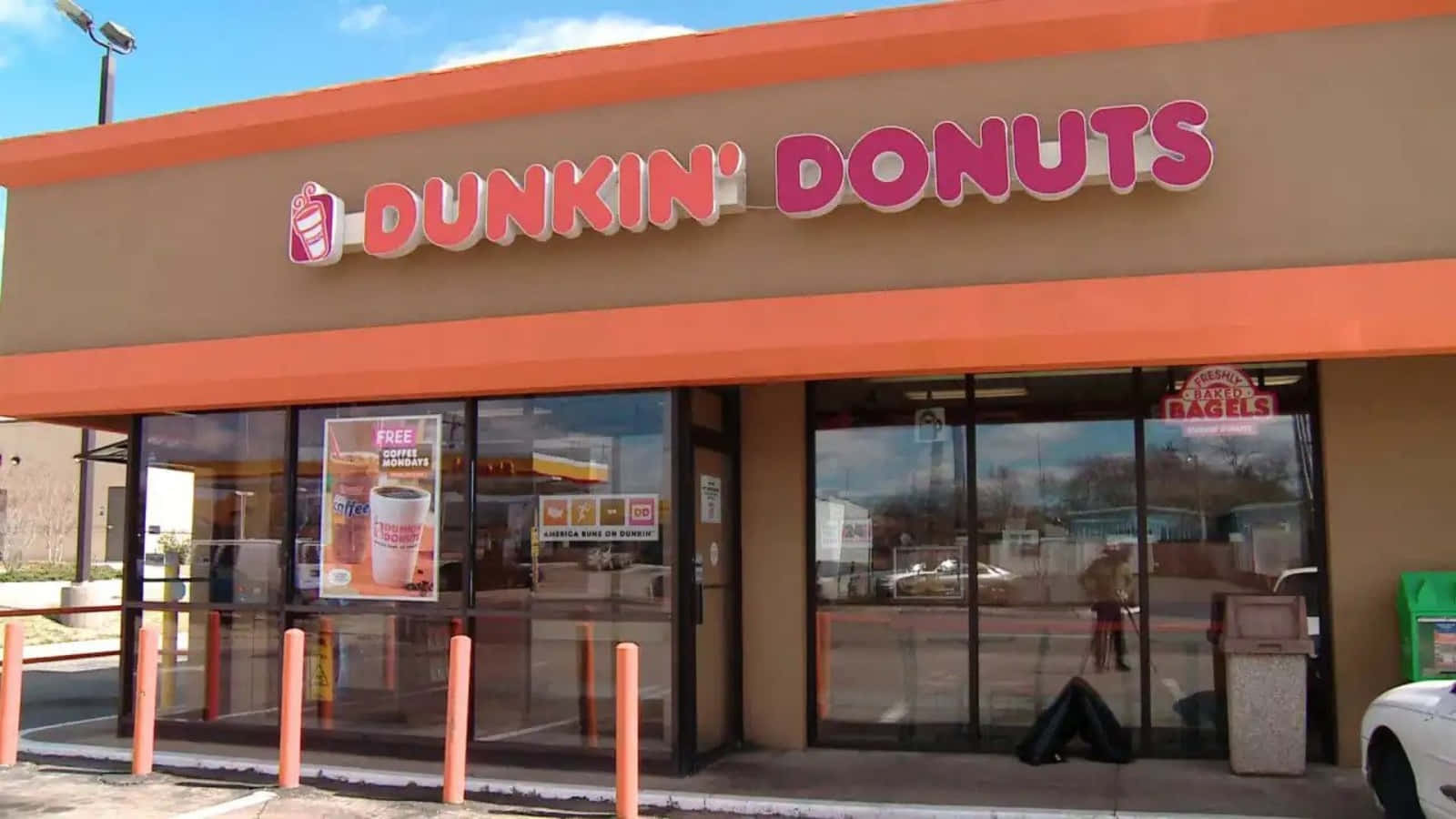 Dunkin Donuts 桌布 壁紙 — 明亮的橙色和棕色Dunkin' Donuts店面，玻璃窗反射出清澈的藍天和經過的汽車。