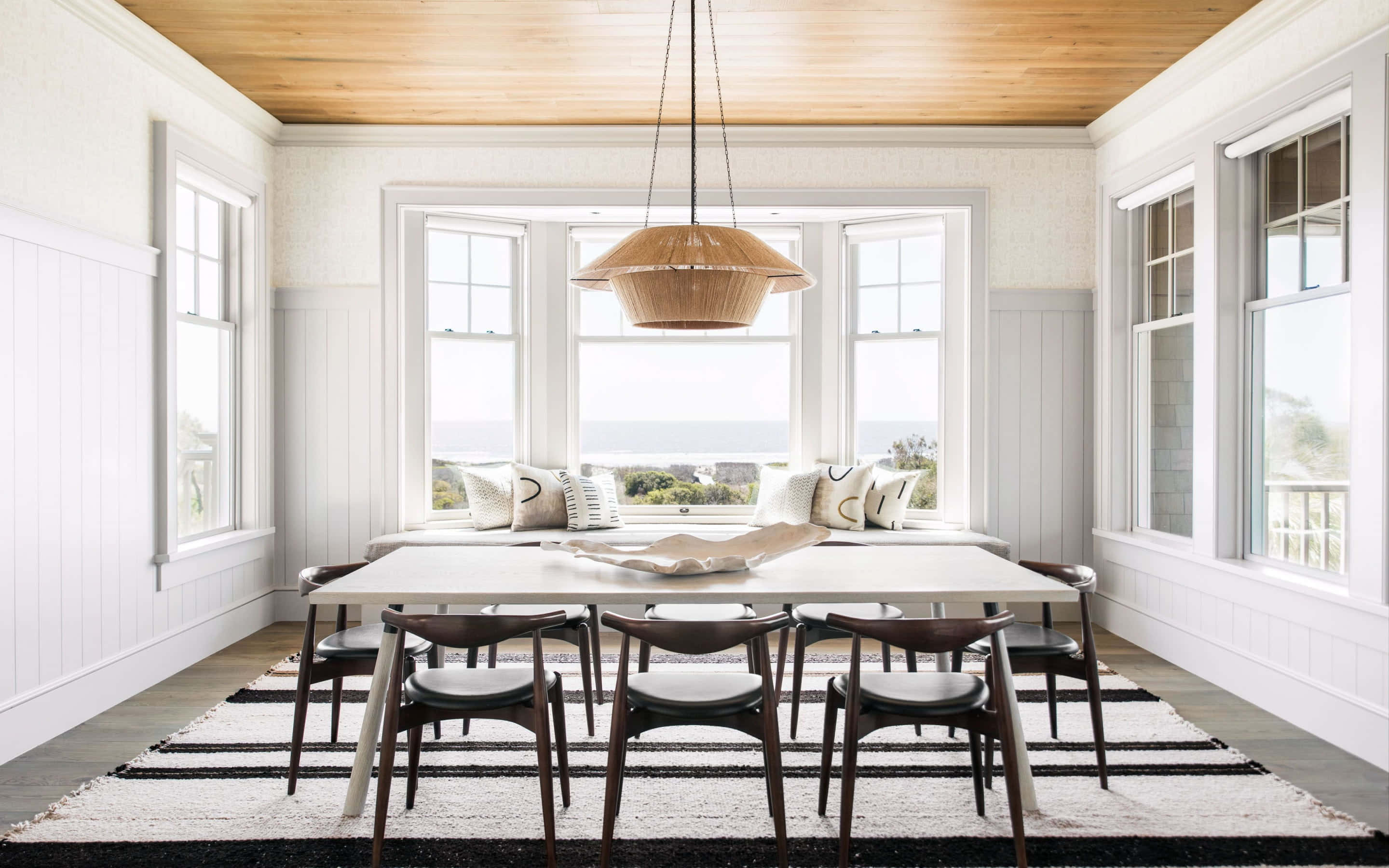 Dining Room 桌布 壁紙 — 明亮的沿海餐廳，白色牆壁、木質天花板和可俯瞰海洋的大窗戶。