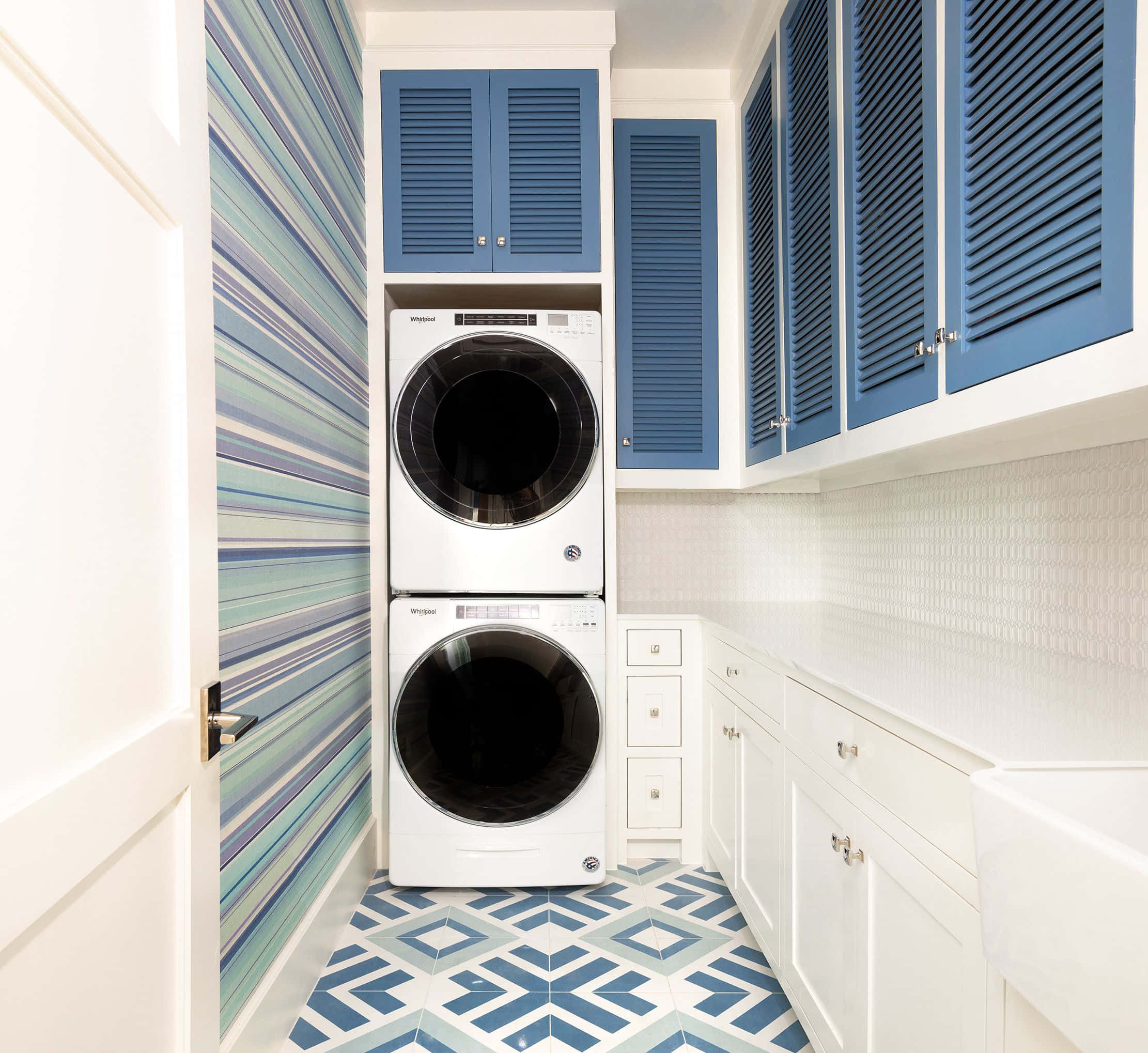 Laundry Room 桌布 壁紙 — 明亮的洗衣房，配有疊放的洗衣機和乾衣機、白色櫥櫃和藍色百葉門，搭配條紋壁紙和幾何瓷磚地板。
