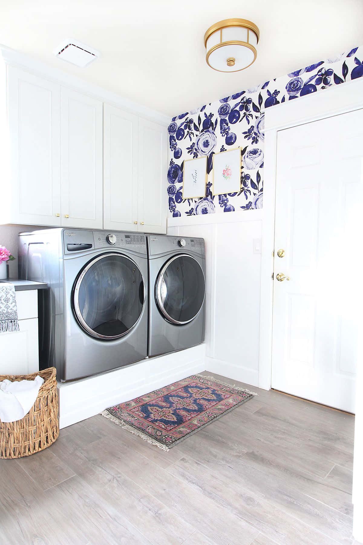 Laundry Room 桌布 壁紙 — 明亮的洗衣房，配有銀色前置式洗衣機、白色櫥櫃和一面大膽的藍色花卉壁紙特色牆。