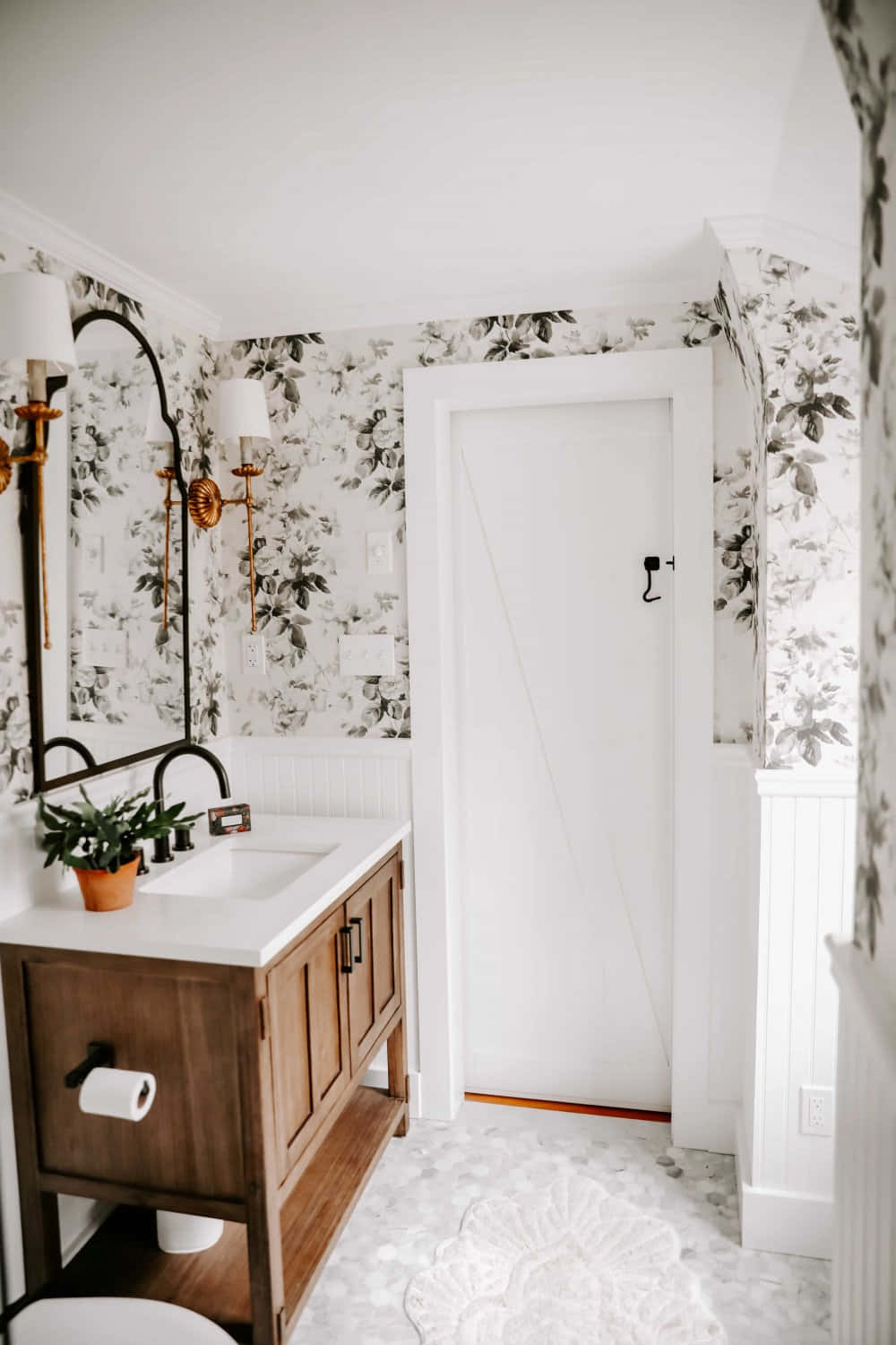 Bathroom Decor 桌布 壁紙 — 明亮的浴室，配有白色花卉壁紙、木製梳妝台和黑色配件，在柔和自然光下。