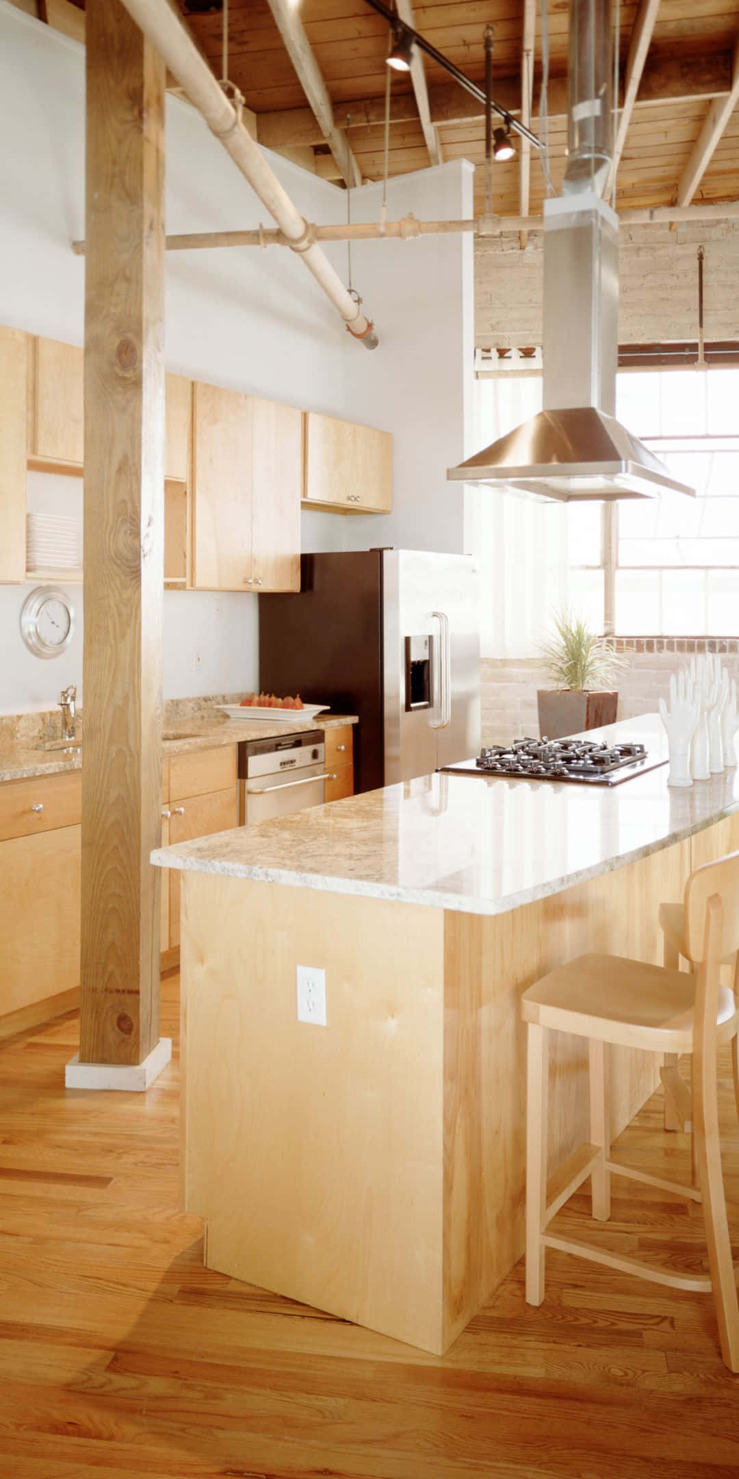 Pixel 3 Kitchen 桌布 壁紙 — 明亮的現代廚房，配有淺色木櫥櫃、硬木地板和裸露的天花板橫樑，中央島台設有大理石檯面和不銹鋼抽油煙機。