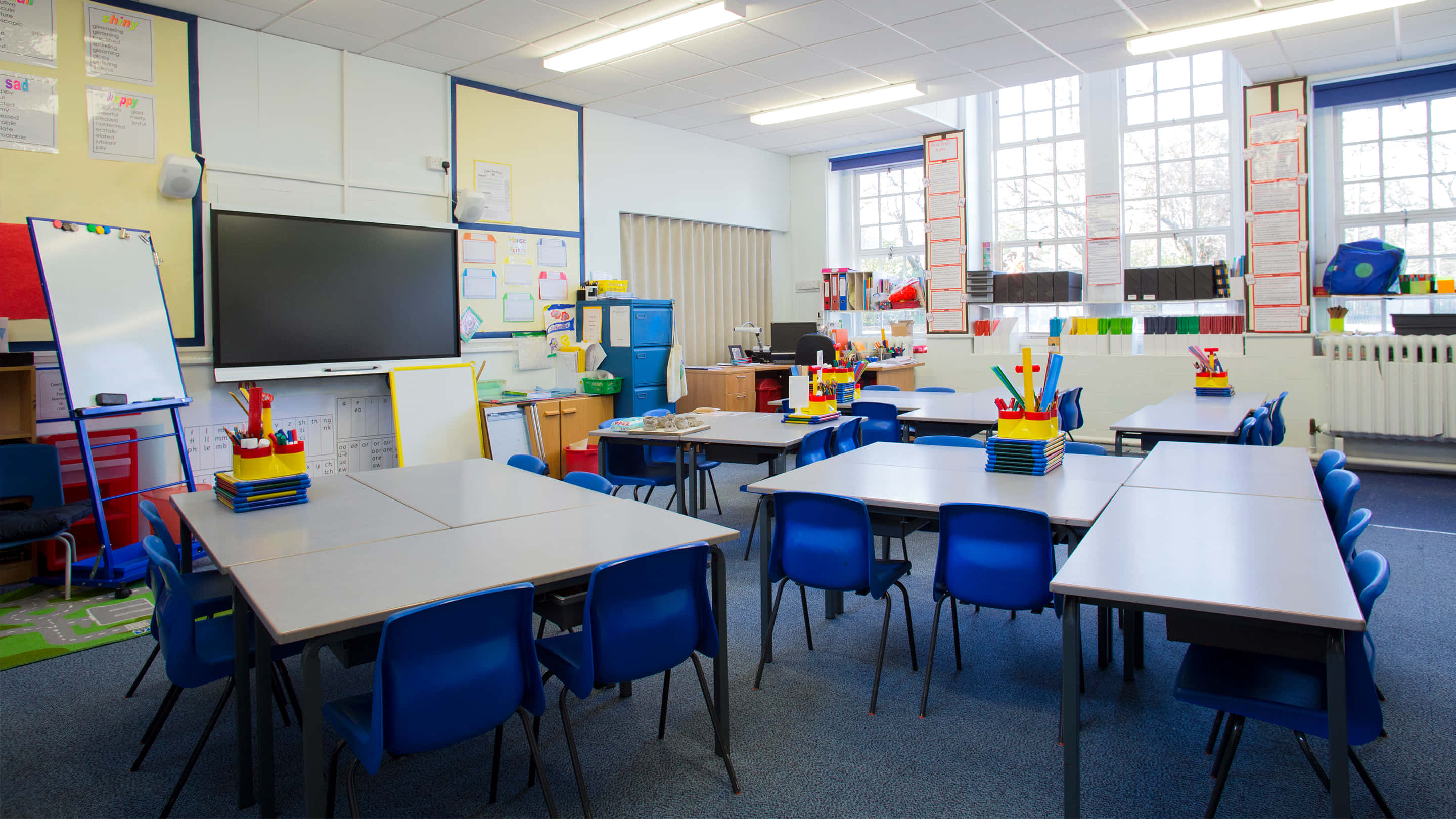 Classroom 桌布 壁紙 — 明亮的現代教室，配有藍色椅子、桌子、白板和讓自然光透入的大窗戶。