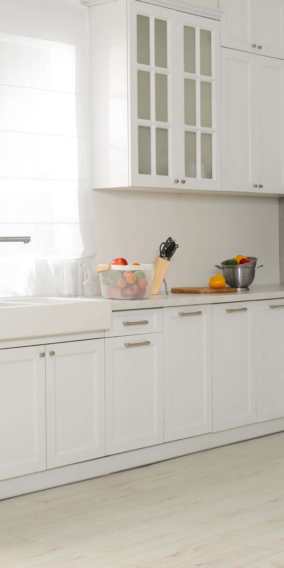 Pixel 3 Kitchen 桌布 壁紙 — 明亮的白色廚房，配有玻璃門櫥櫃，自然光線照亮檯面上的新鮮水果。