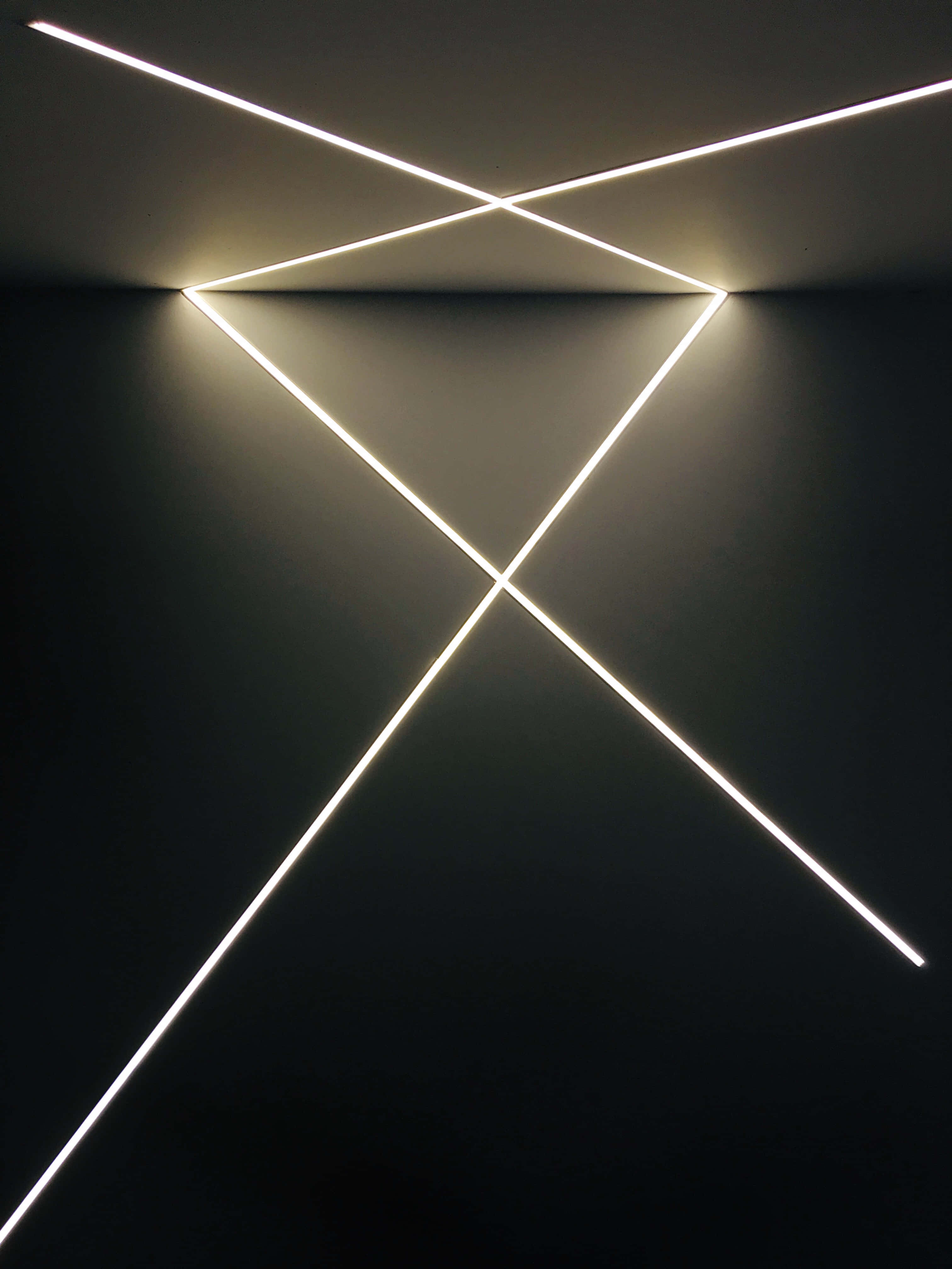 LED 桌布 壁紙 — 明亮的白色霓虹燈管在黑暗的極簡主義天花板和牆壁上形成交叉的幾何線條。
