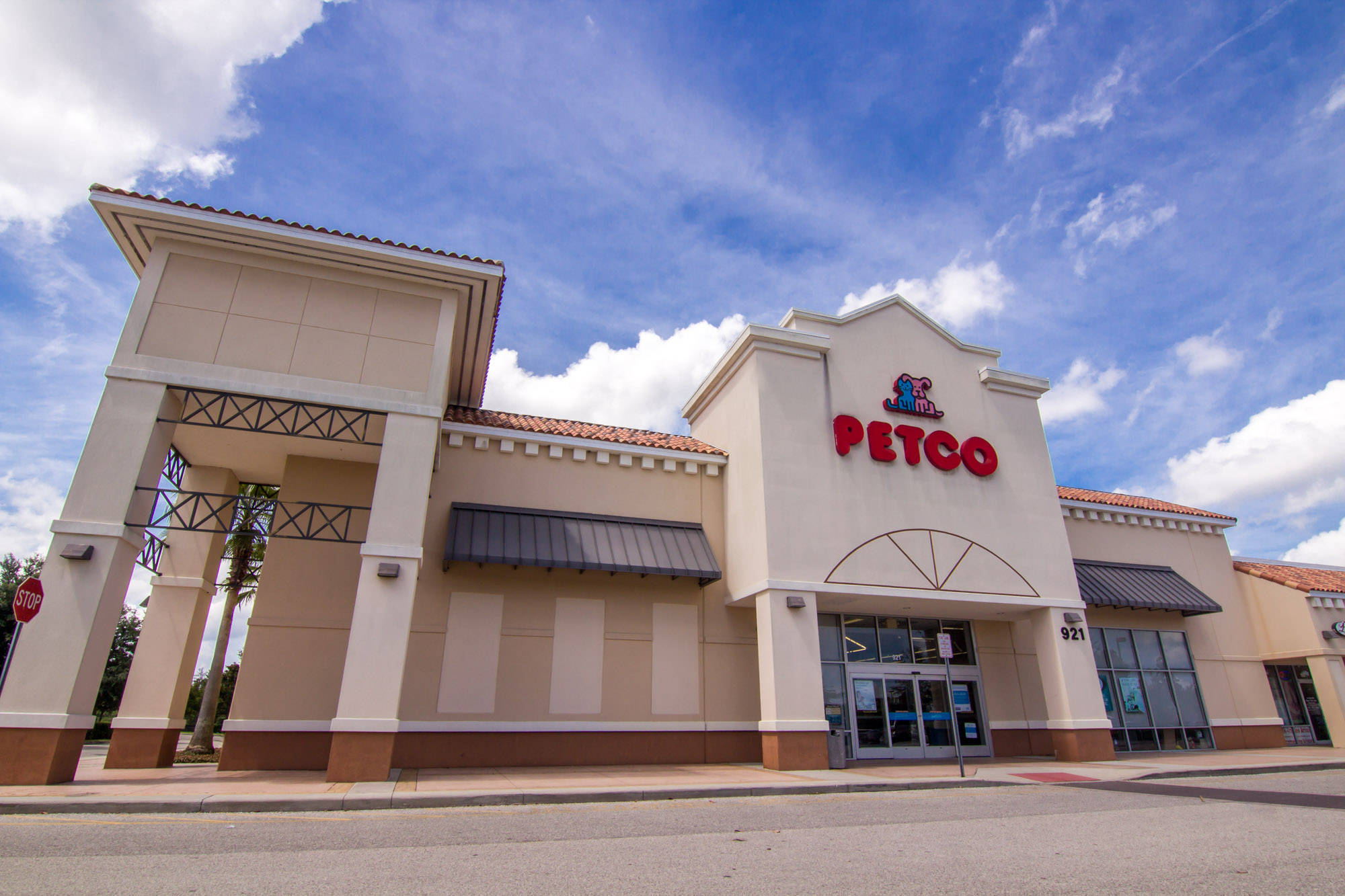 Orange City 桌布 壁紙 — 明亮的藍天白雲籠罩著米色 Petco 商店，帶有紅色招牌和瓷磚屋頂裝飾。