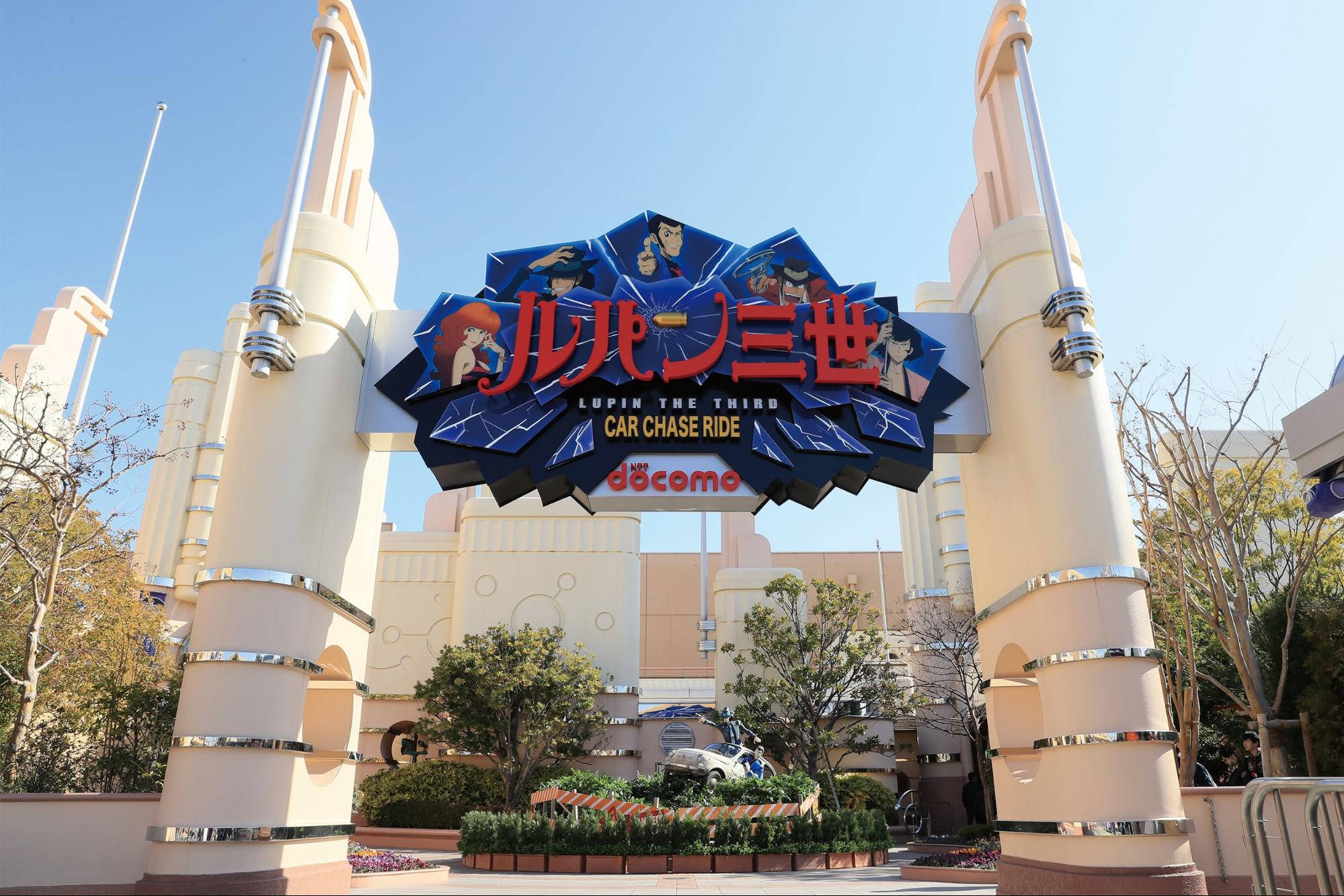 Universal 桌布 壁紙 — 明亮的藍天襯托著主題公園中《魯邦三世》汽車追逐之旅的宏偉入口，配有醒目的標誌和奶油色柱子。