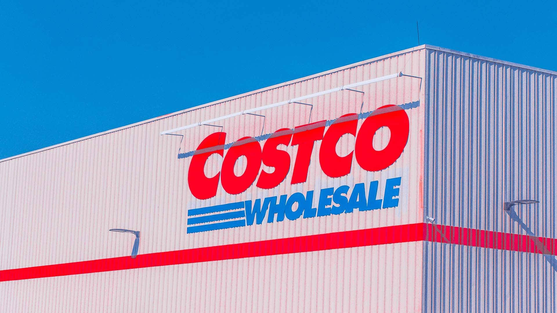 Costco 桌布 壁紙 — 明亮的藍天襯托著大型米色倉庫建築上醒目的紅色和藍色Costco Wholesale標誌。