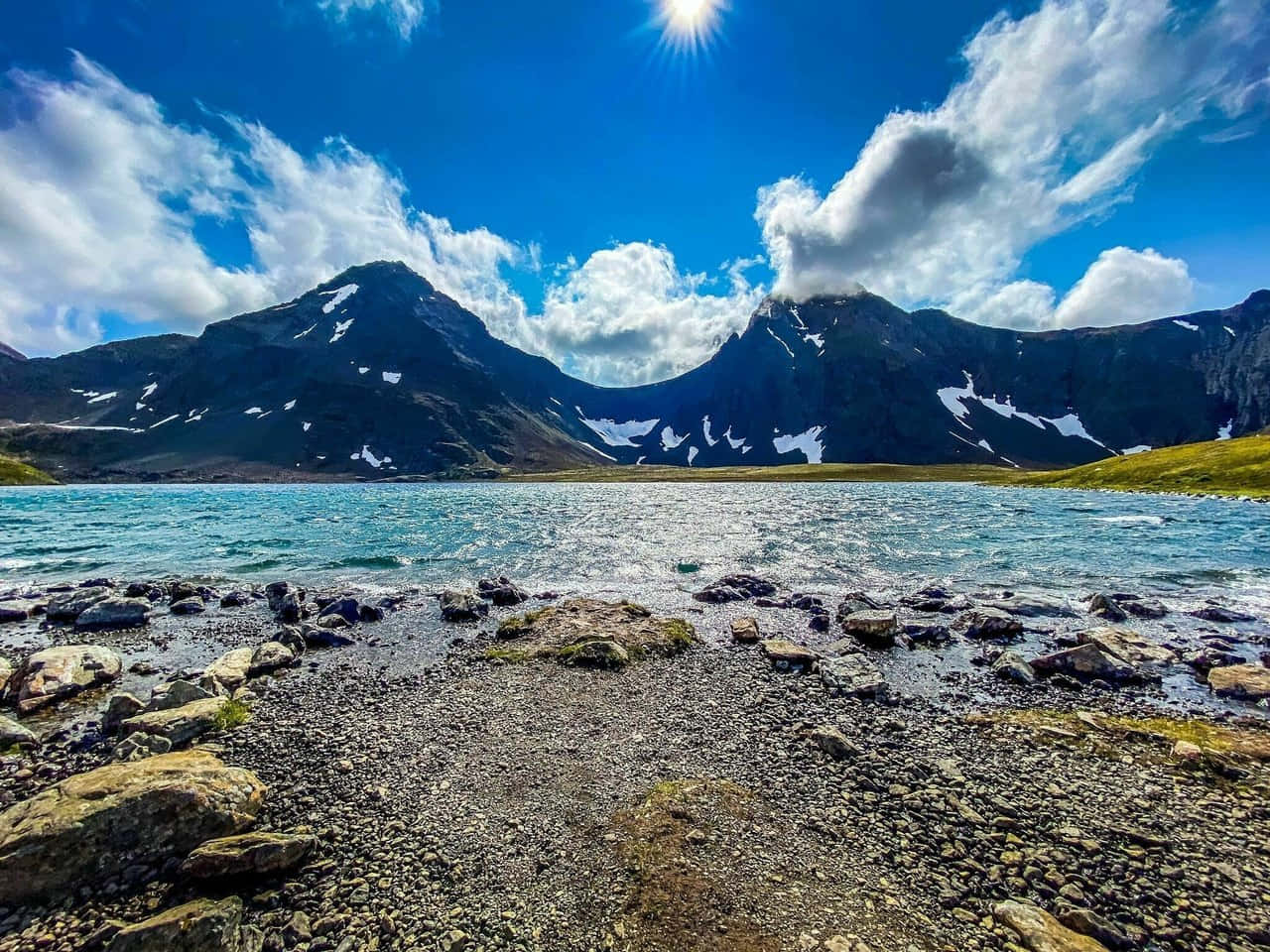 Mountain Scenery 桌布 壁紙 — 明亮的陽光照耀著一個藍綠色的湖泊，周圍是白雪覆蓋的山脈和岩石海岸，藍天白雲。