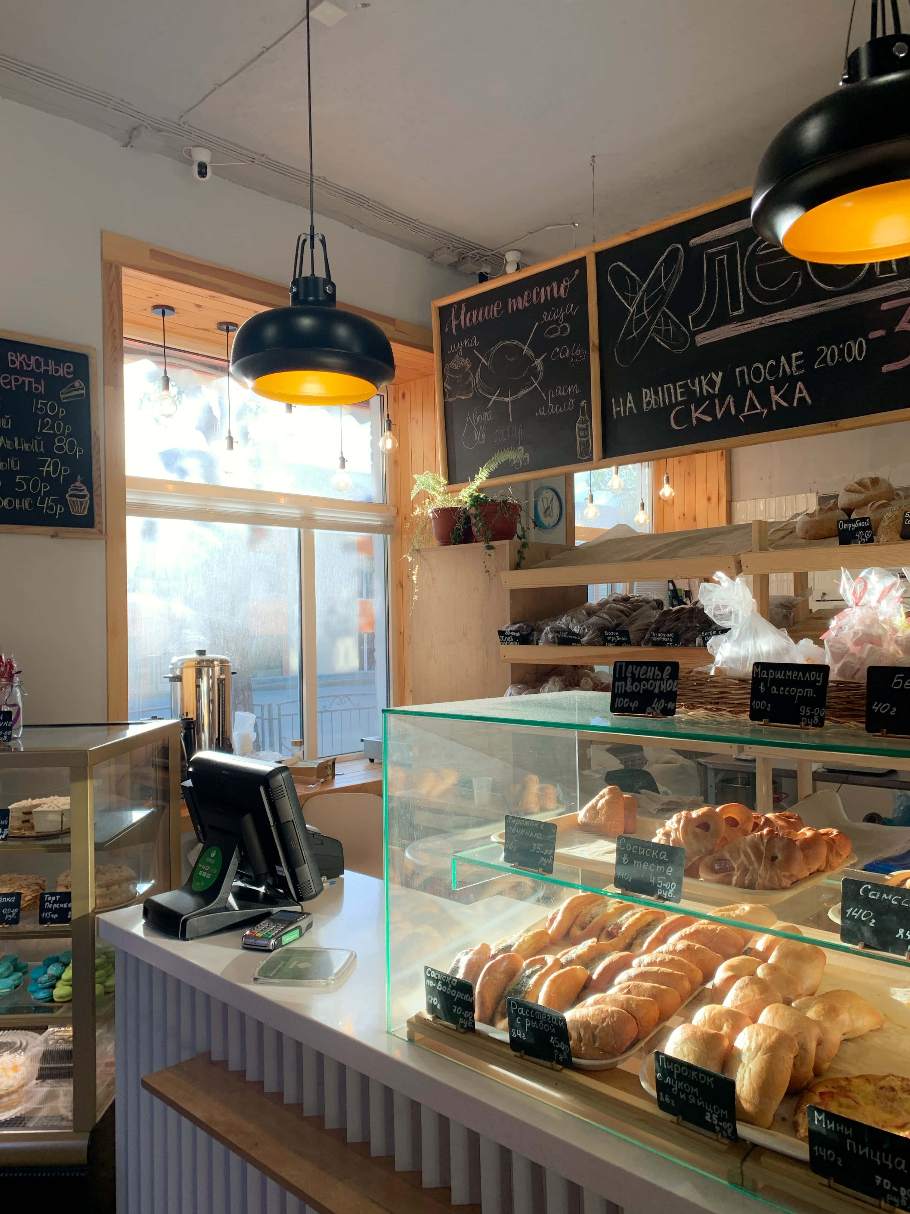 Bakery 桌布 壁紙 — 明亮的麵包店內部，玻璃展示櫃裝滿新鮮麵包和糕點，在溫暖的吊燈下。