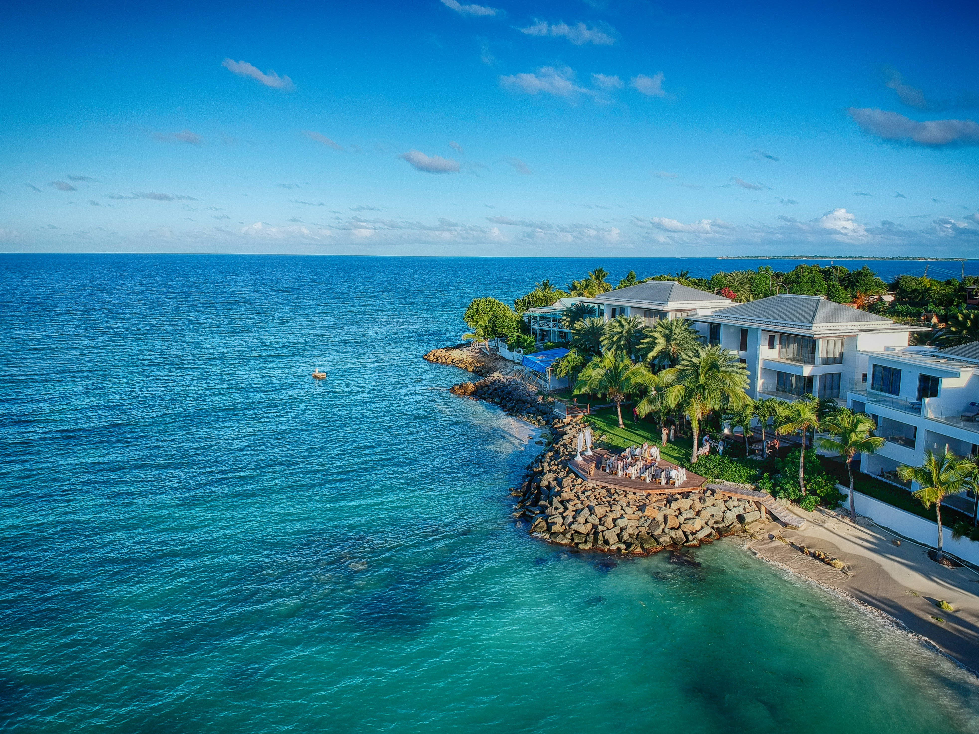 Antigua And Barbuda 桌布 壁紙 — 明亮藍天下，棕櫚樹間豪華海岸住宅與碧綠海水的鳥瞰圖。