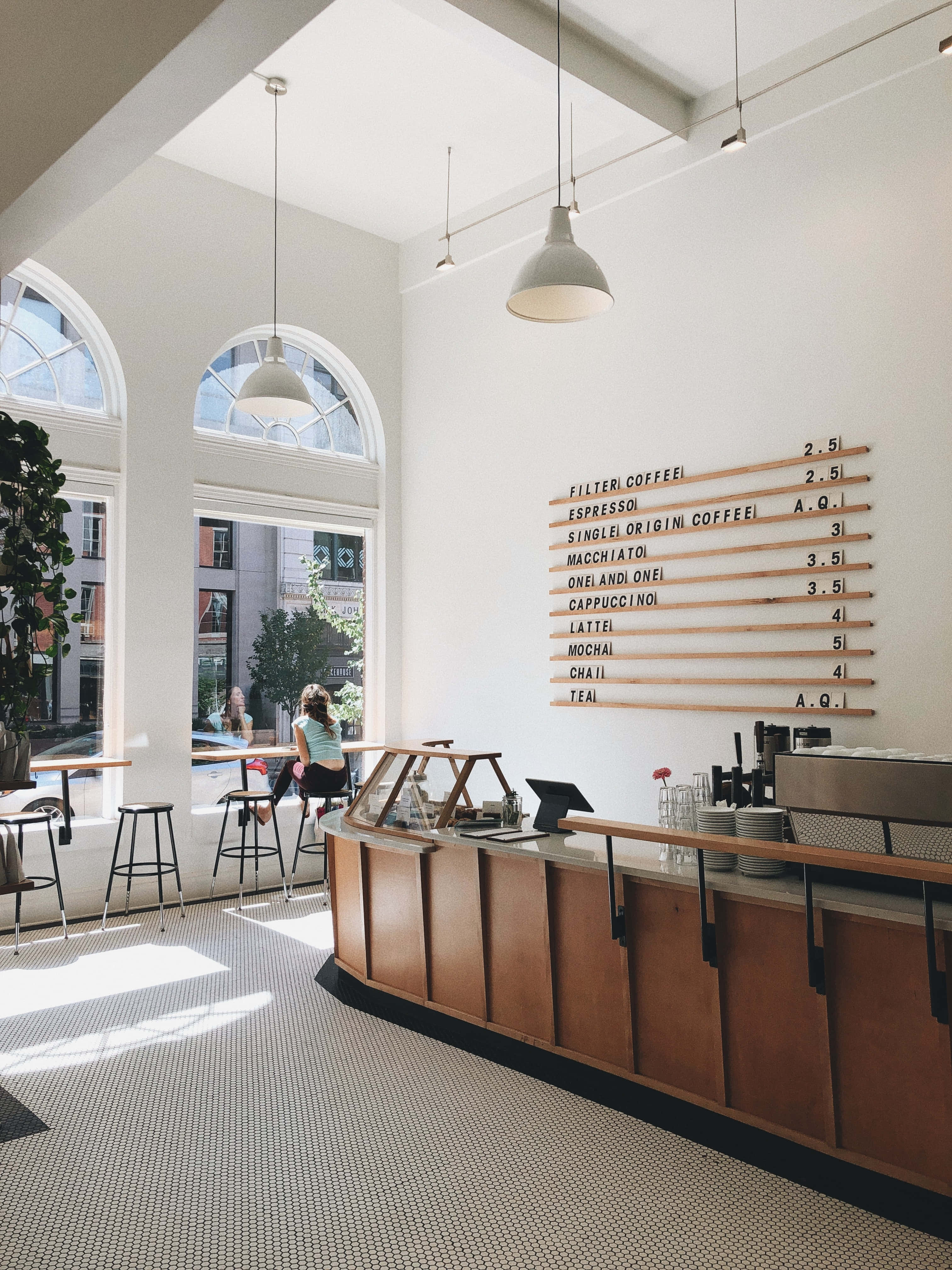 Coffee Aesthetic 桌布 壁紙 — 明亮通風的咖啡店，白色牆壁、木製櫃檯和拱形窗戶，讓自然光線透入。