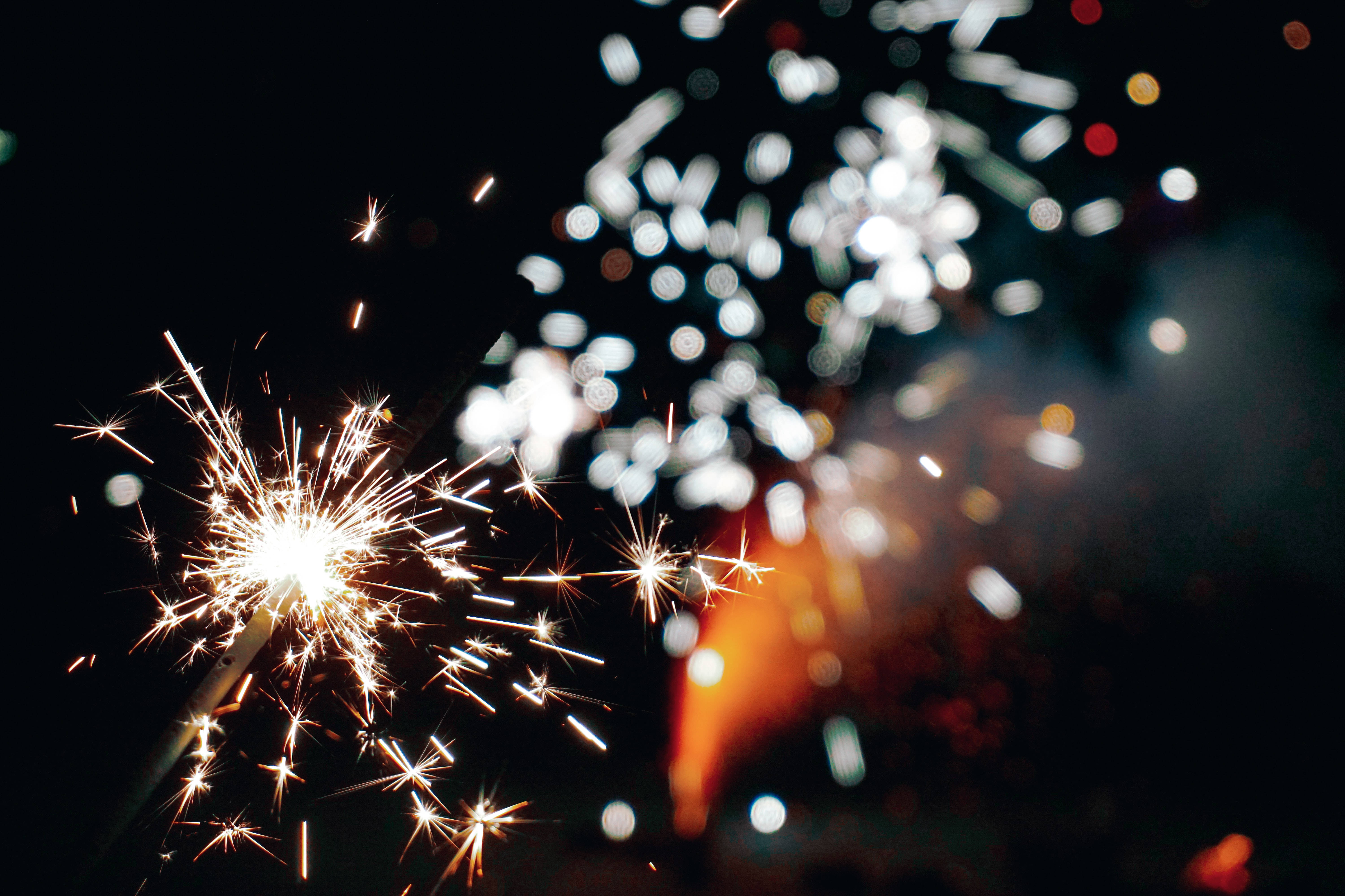 sparklers 桌布 壁紙 — 明亮閃爍的煙火在漆黑的夜空中爆炸，背景是模糊的散景燈光。