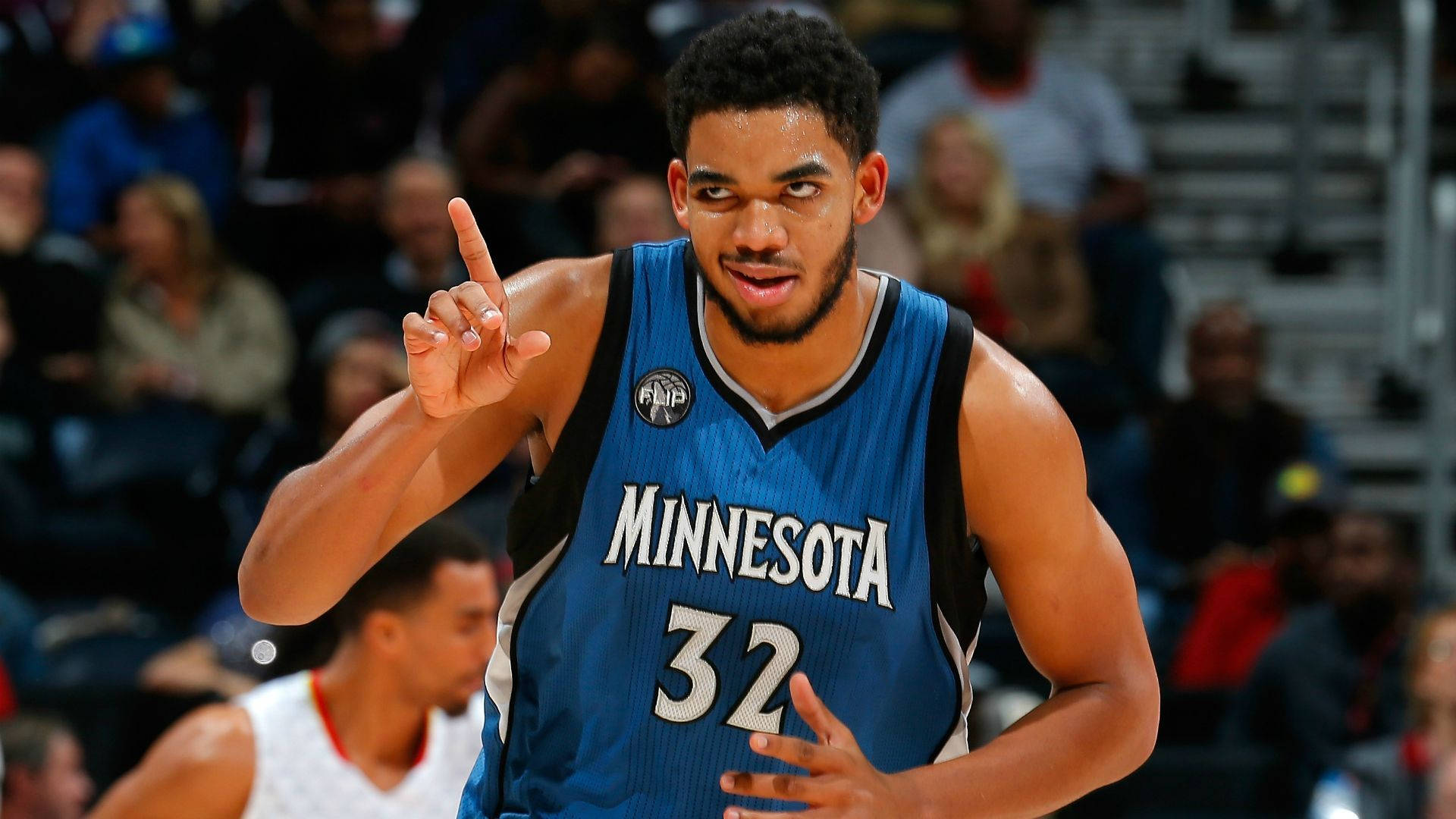 karl-anthony towns 桌布 壁紙 — 明尼蘇達灰狼隊專注的籃球運動員身穿藍色32號球衣，在比賽中舉起一根手指做手勢。