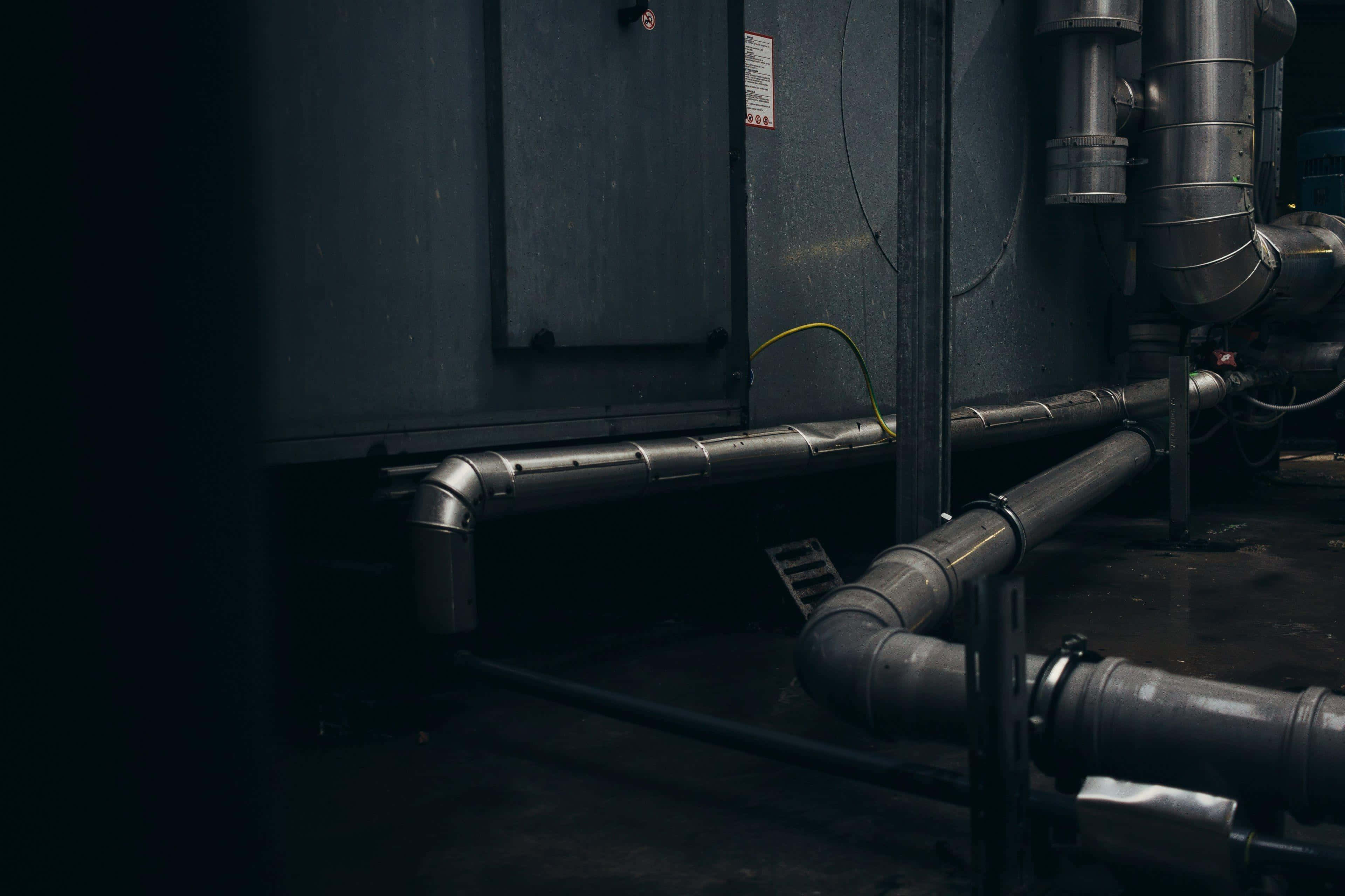 Plumbing 桌布 壁紙 — 昏暗機械室內的工業管道和機械，帶有鮮明的陰影和金屬質感。