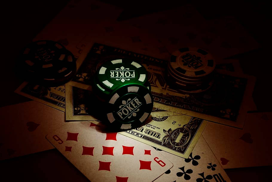 Dice 桌布 壁紙 — 昏暗燈光下的籌碼和撲克牌散落在美元鈔票上，營造出陰暗的賭博場景。
