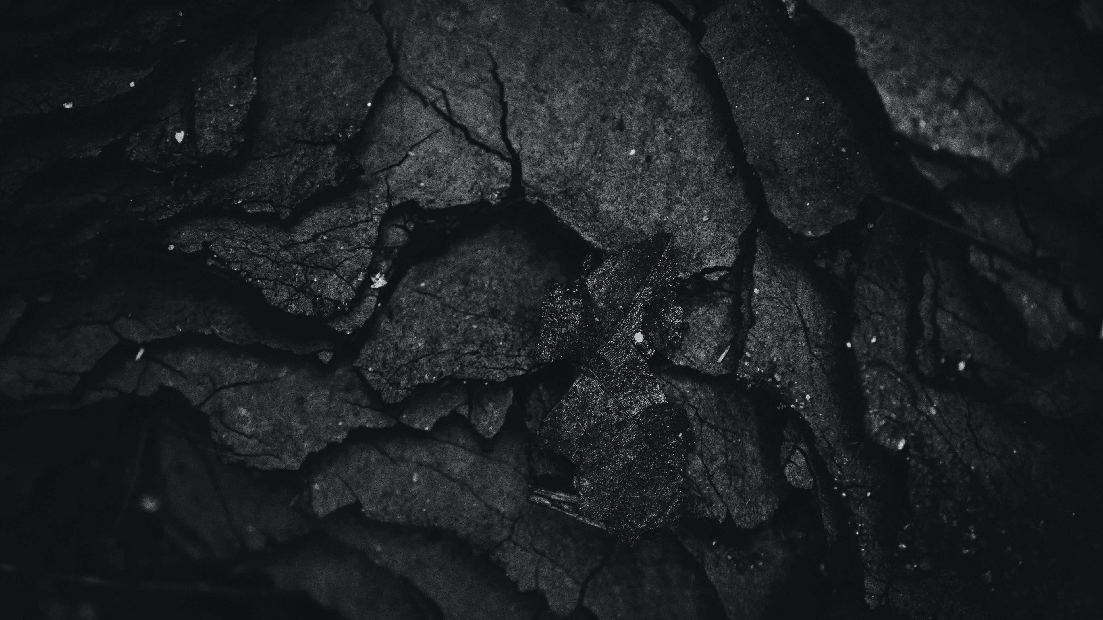 Dark Rock 桌布 壁紙 — 昏暗燈光下裂開黑色木炭的特寫，帶有細微灰色紋理和散落的白色斑點。