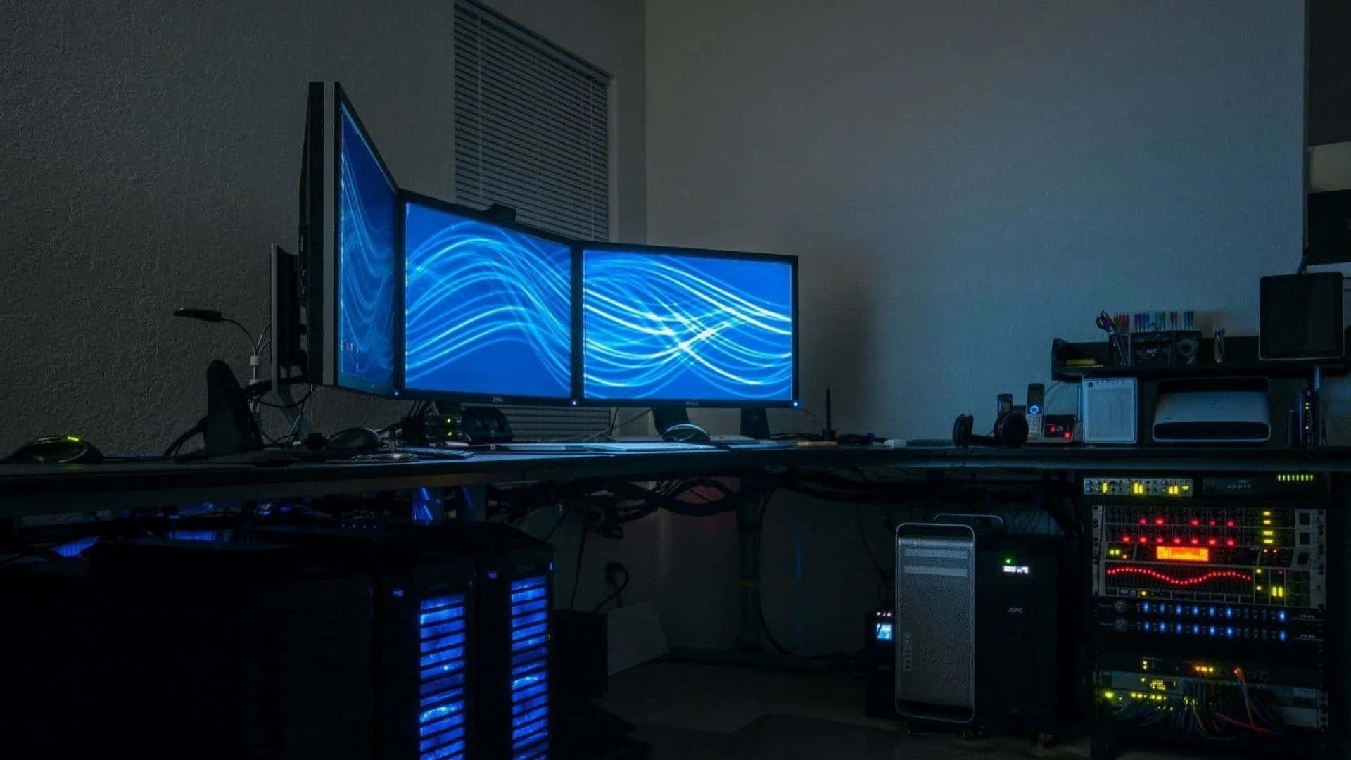 Gaming Room 桌布 壁紙 — 昏暗燈光的遊戲設置，三個顯示器顯示藍色波浪桌布，以及發光的RGB燈光電腦主機。