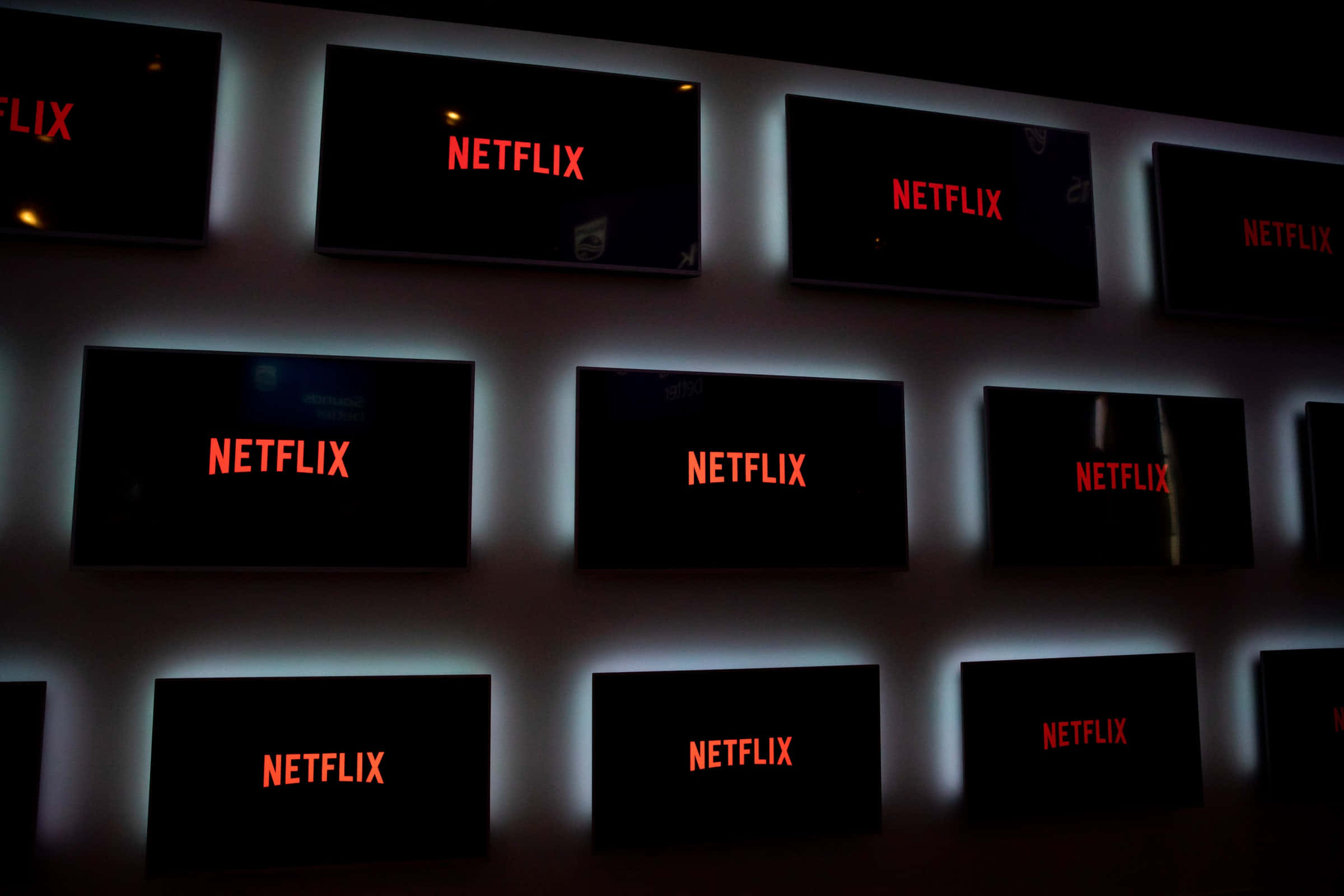 Netflix 桌布 壁紙 — 昏暗的牆壁上顯示多個發光的 Netflix 標誌，螢幕帶有藍色背光。