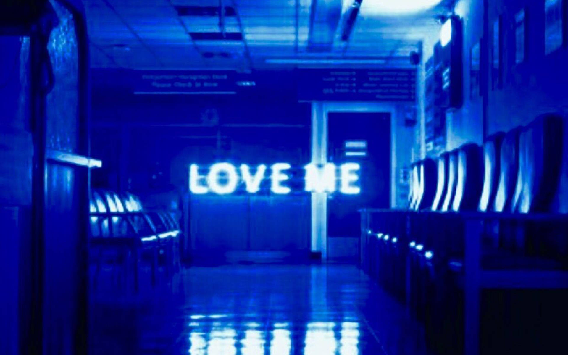blue aesthetic pc 桌布 壁紙 — 昏暗的藍色醫院走廊，發光的「LOVE ME」標誌在濕漉漉的地板上反射，兩旁是一排排椅子。