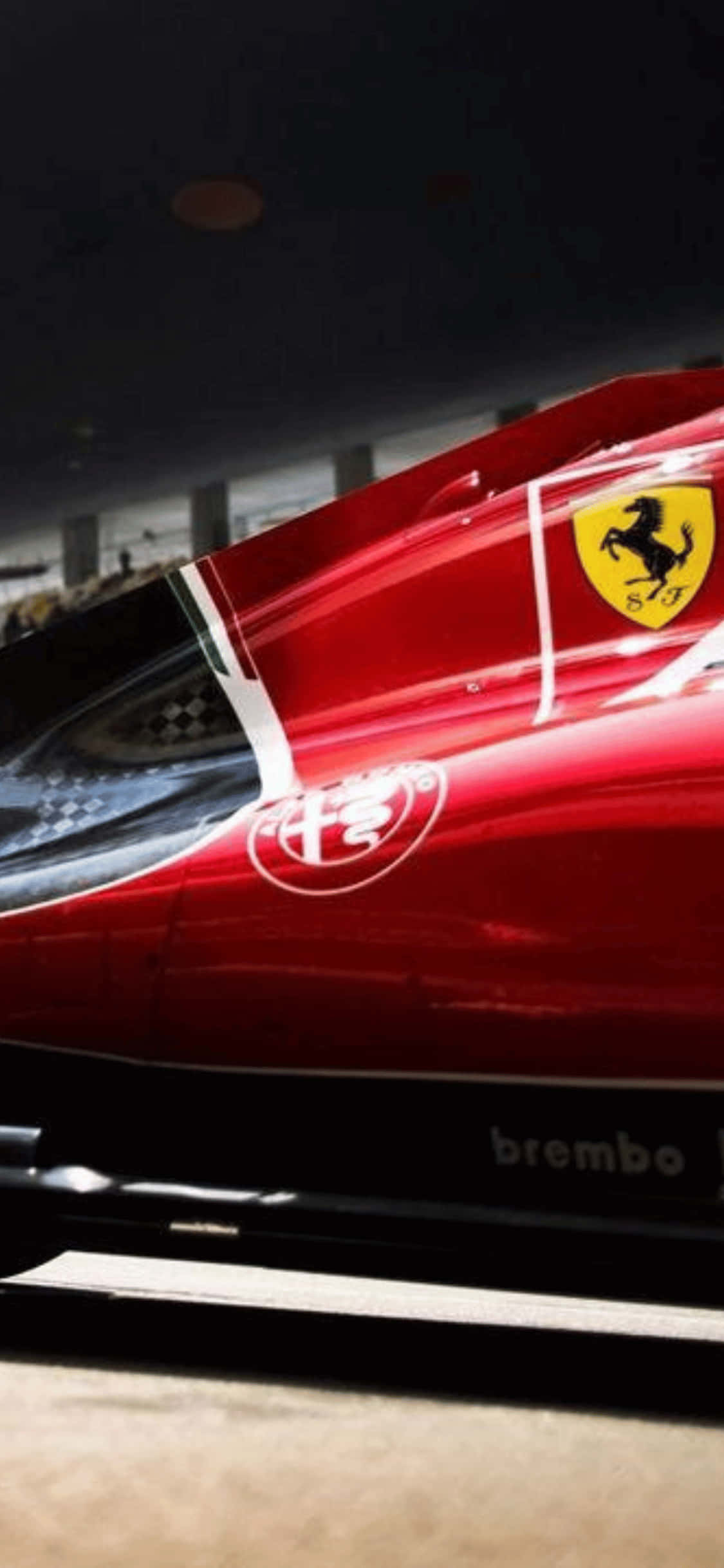F1 2018 桌布 壁紙 — 昏暗車庫燈光下，一輛亮紅色法拉利F1賽車的特寫，帶有黃色躍馬標誌。