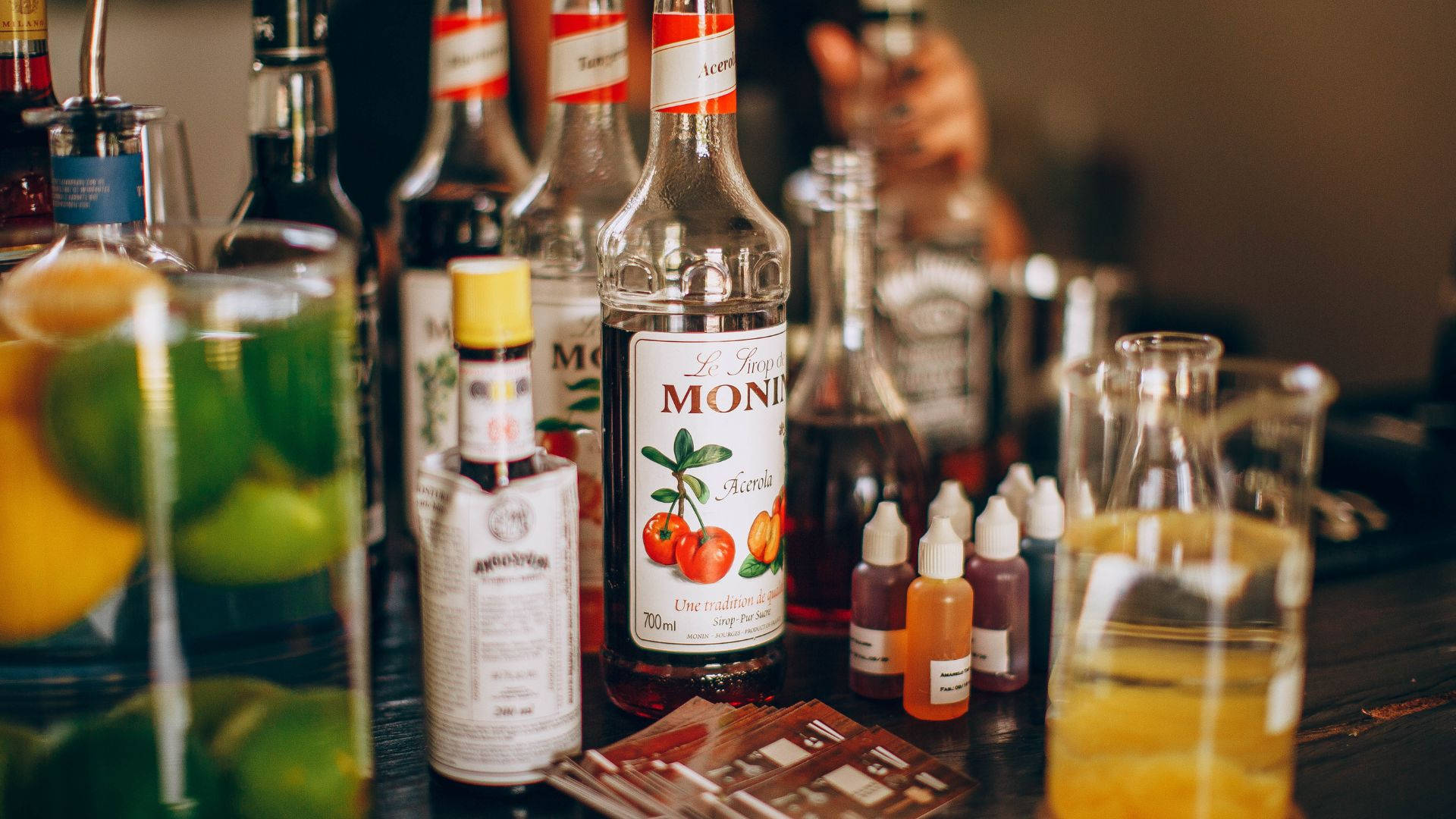 alcohol 桌布 壁紙 — 昏暗酒吧櫃檯的特寫，有酒瓶、柑橘裝飾和雞尾酒調酒器，營造出溫馨誘人的氛圍。