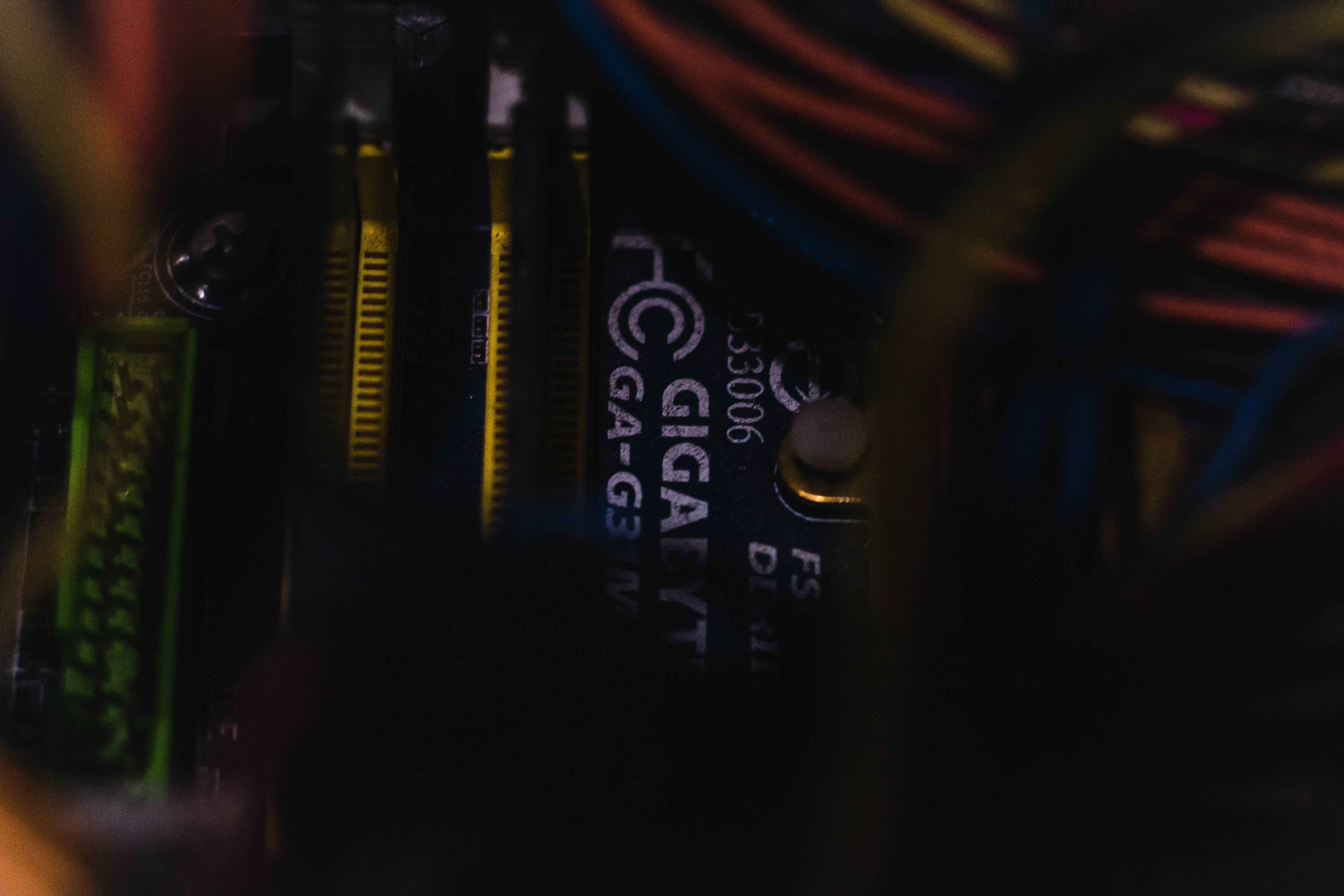 Motherboard 桌布 壁紙 — 昏暗電腦主機板的特寫，帶有彩色電纜和發光的綠色組件。