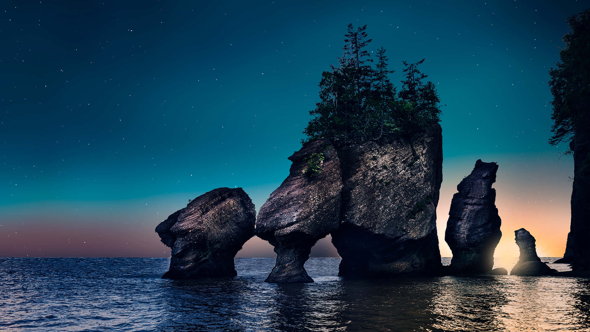 Stone 桌布 壁紙 — 星光下的海蝕柱從平靜的海水中升起，上方是漸變的暮色天空，點綴著星星。